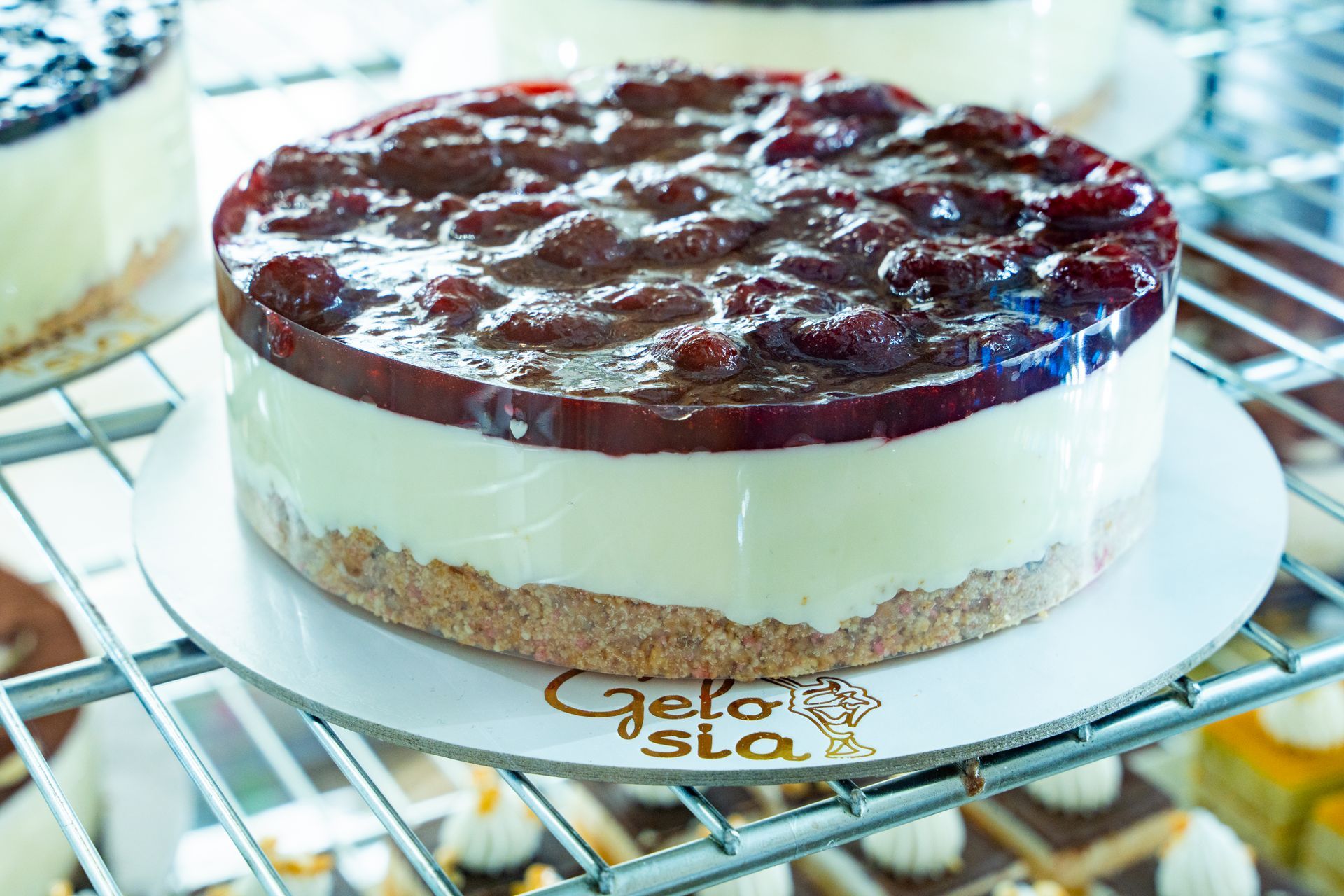Cheesecake rotonda con glassa lucida ai frutti di bosco, presentata su un supporto di vetro.