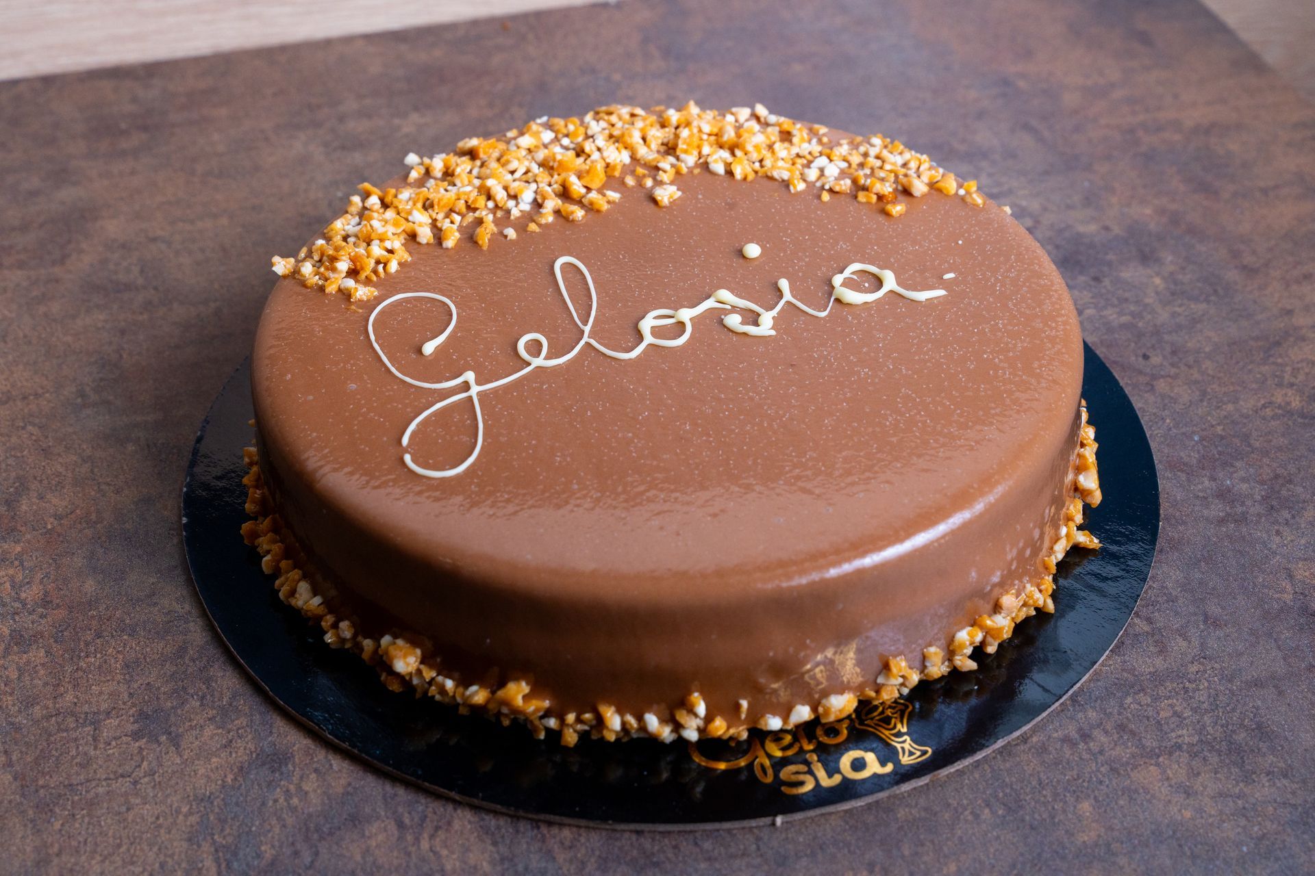 Torta rotonda ricoperta di glassa al cioccolato con granella dorata e la scritta
