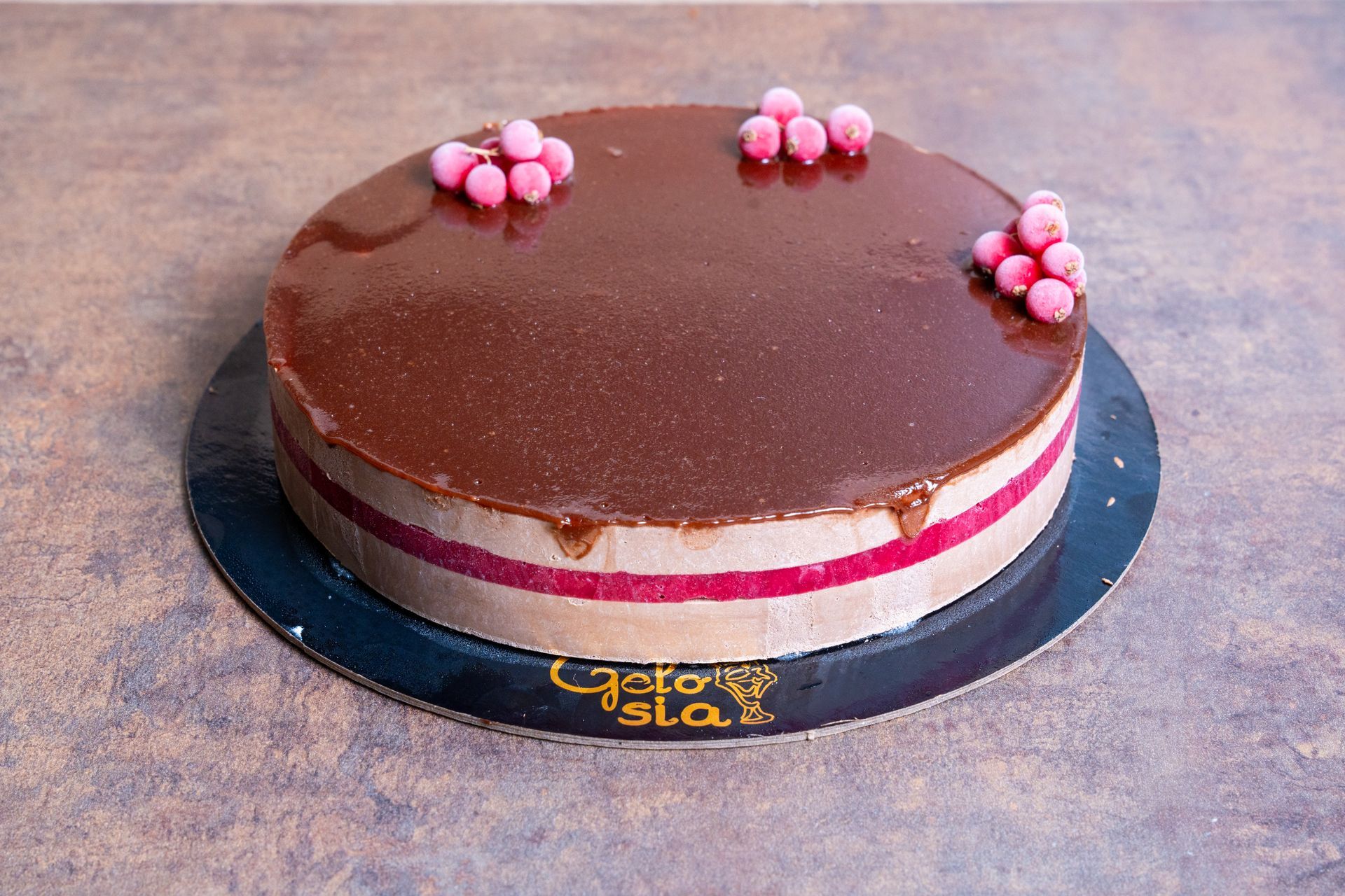 Torta rotonda ricoperta di glassa al cioccolato con ripieno rosa e decorazioni floreali rosa sulla parte superiore, su un vassoio nero.