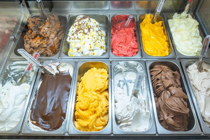 Assortimento di gusti di gelato in contenitori espositivi, tra cui palline di gelato bianco, al cioccolato, giallo, rosa e marrone.