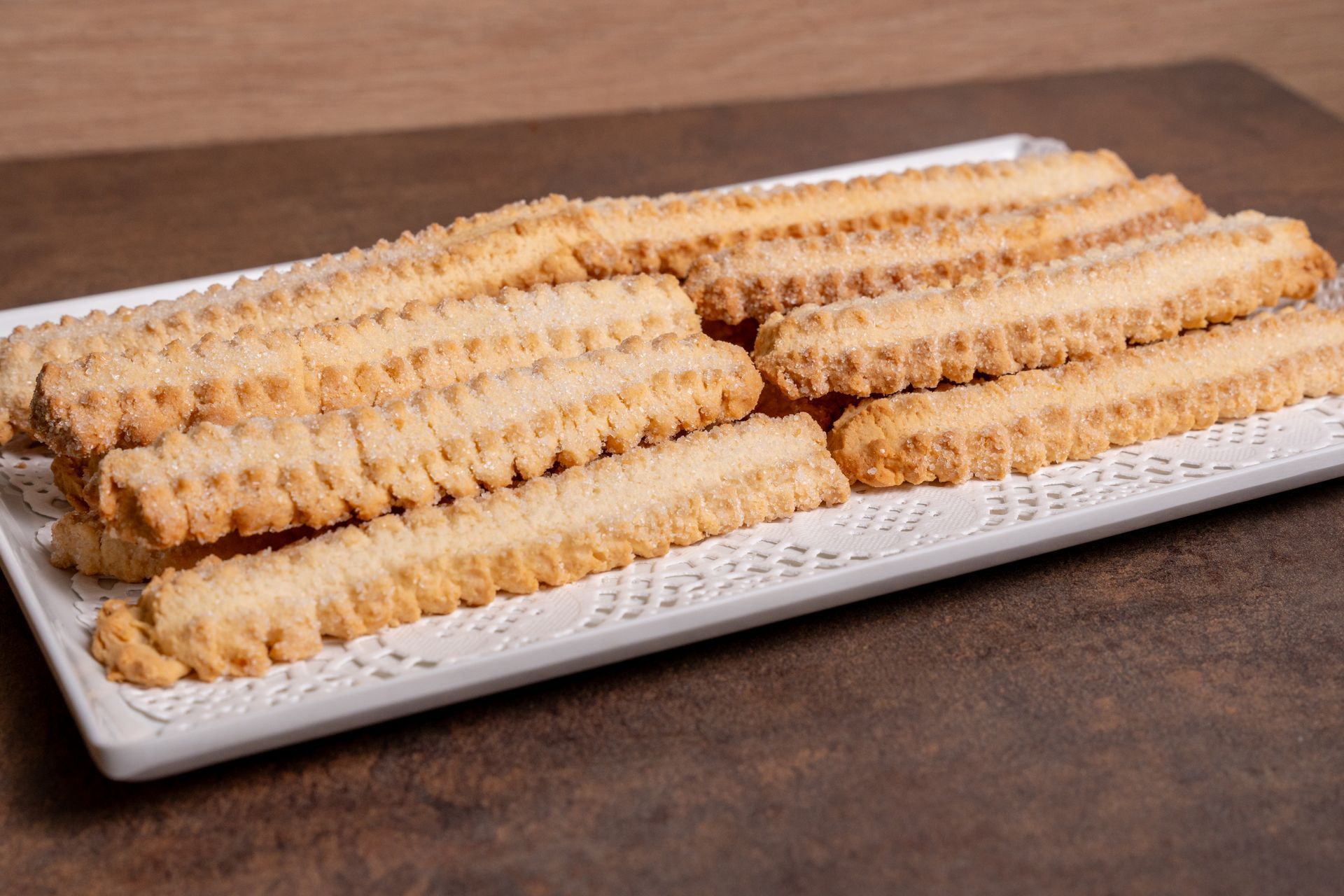 Un vassoio di biscotti waffle dorati su un piatto bianco appoggiato su un tavolo di legno.