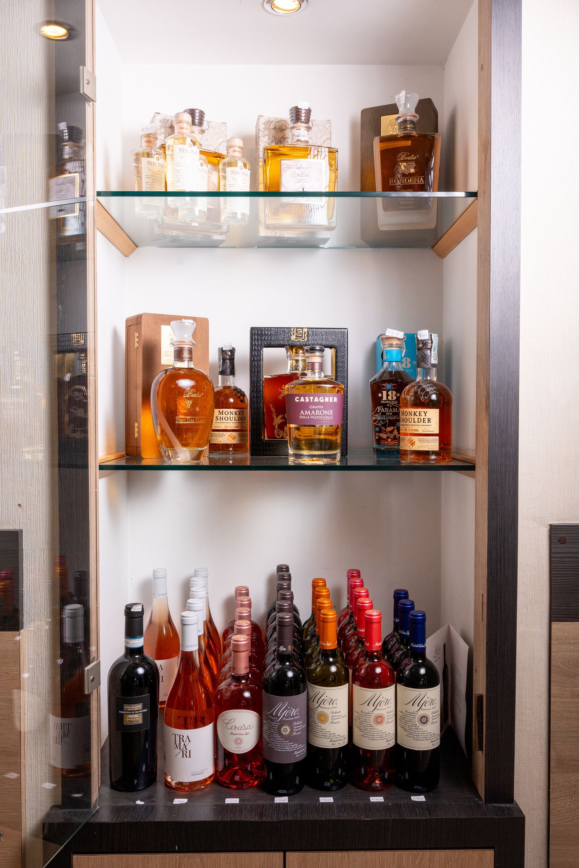 Bottiglie di liquore disposte su ripiani di vetro all'interno di un mobile illuminato.