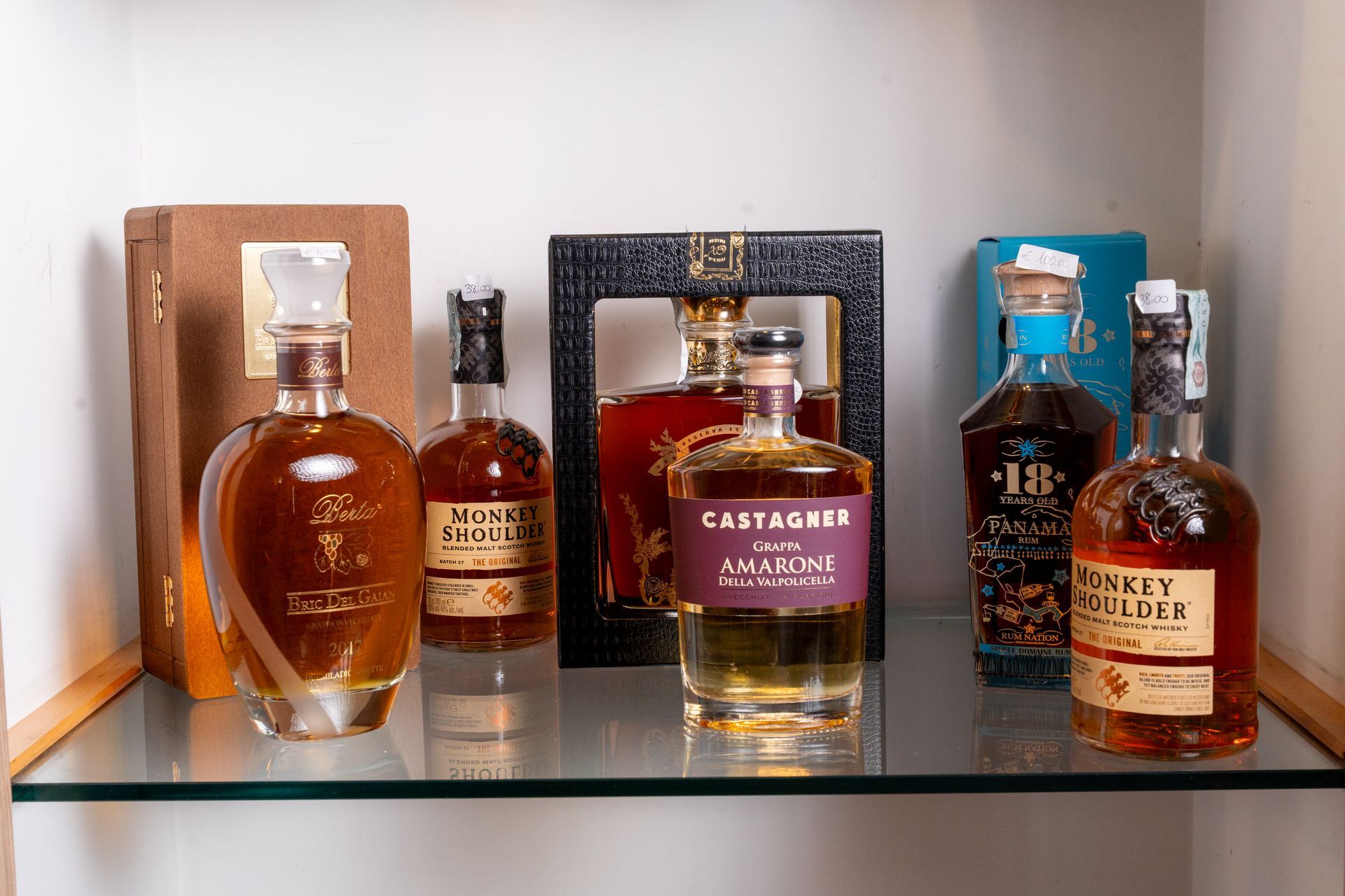 Diverse bottiglie di whisky esposte su una mensola di vetro con sfondi decorativi in ​​legno e scuro.