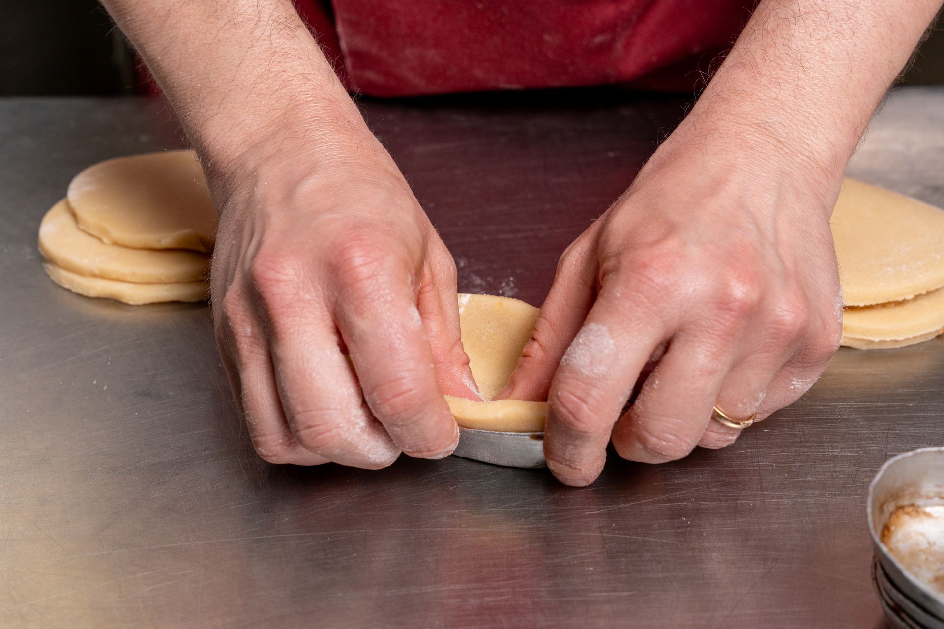 Mani che modellano un disco di pasta per biscotti su un piano di lavoro, con altri dischi di pasta impilati nelle vicinanze.
