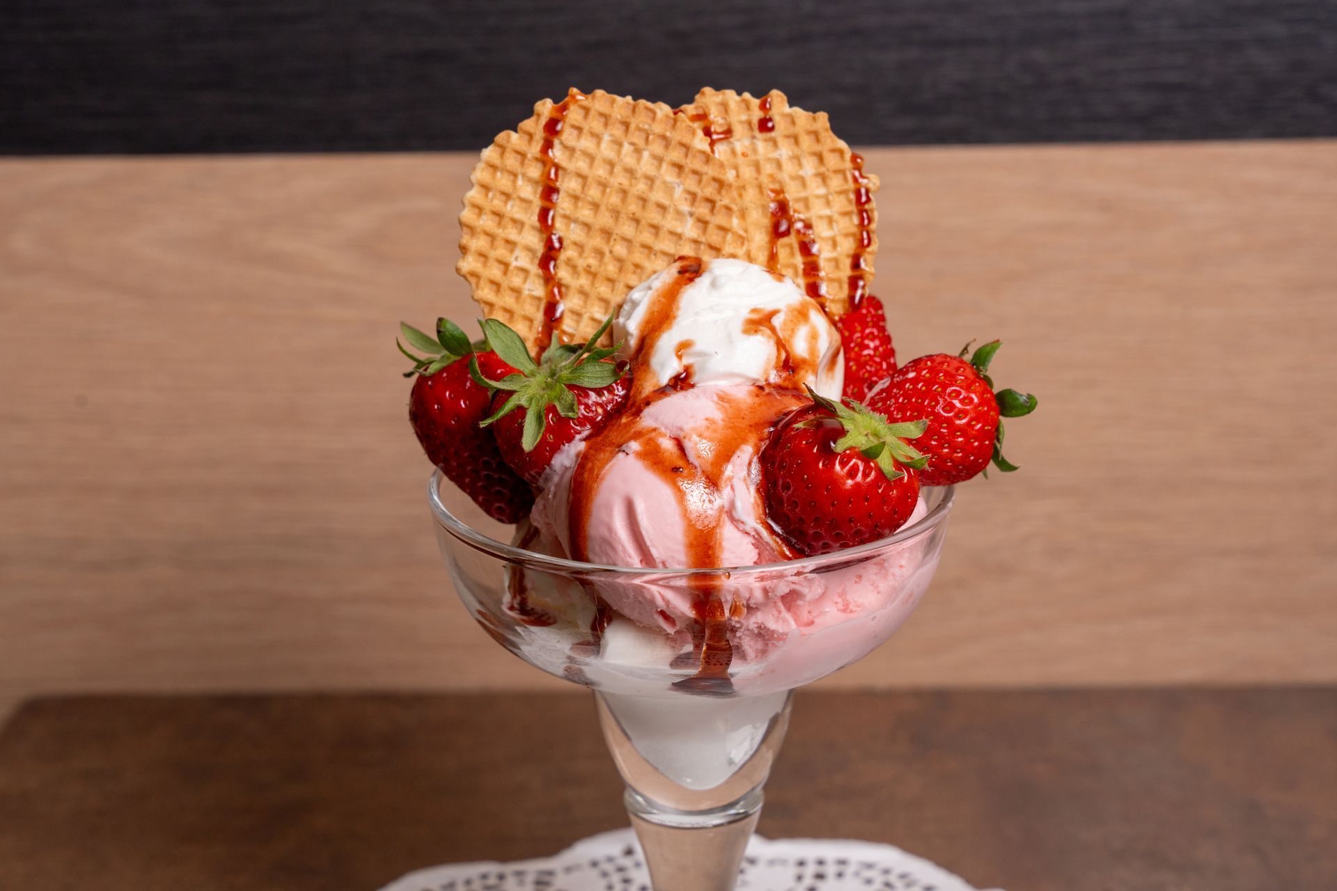 Coppa gelato con fragole, panna montata, salsa al caramello e cialde in una coppetta di vetro.