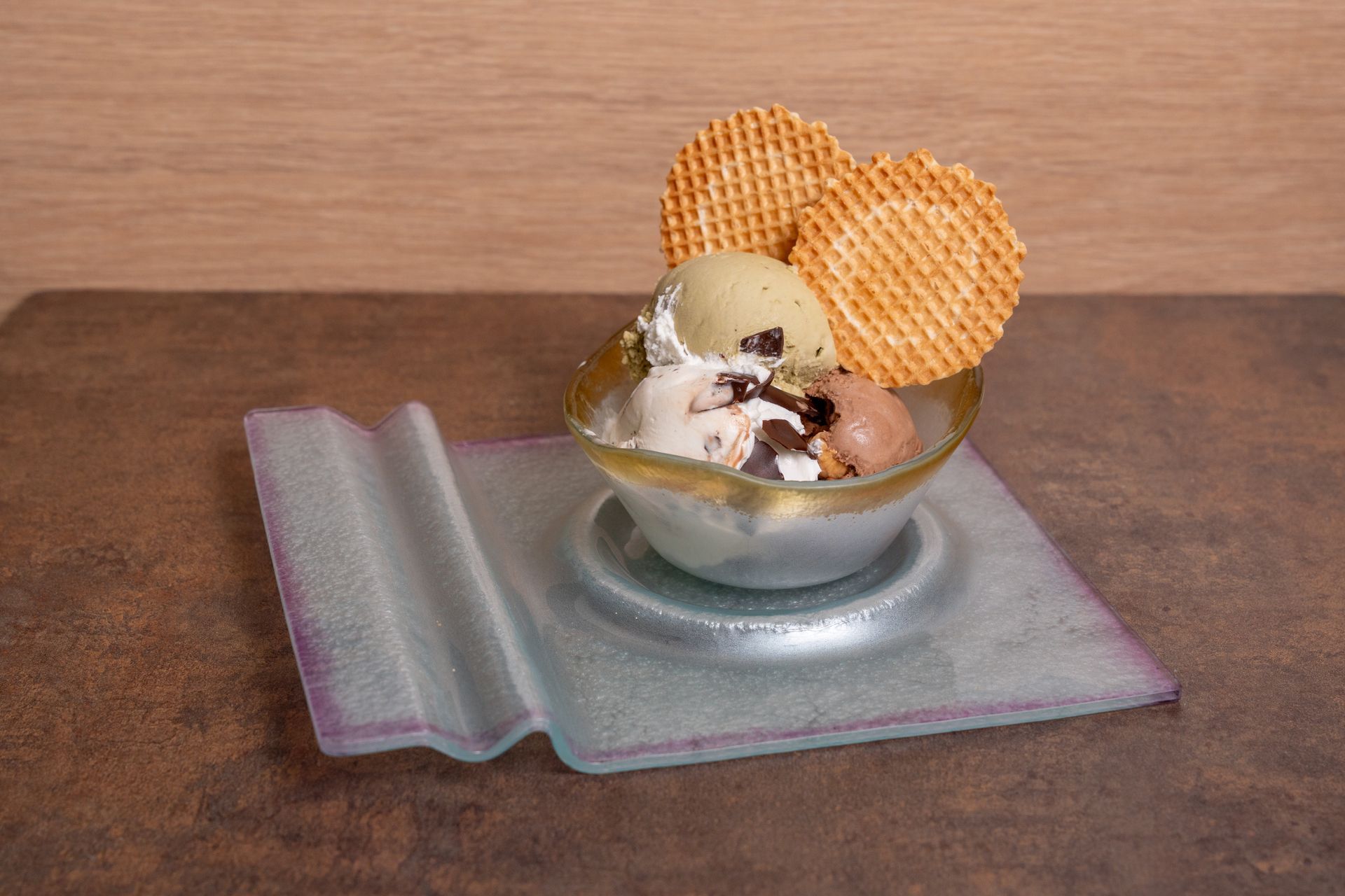 Una coppetta di vetro con gelato e cialde su un tovagliolo piegato, su un tavolo di legno.