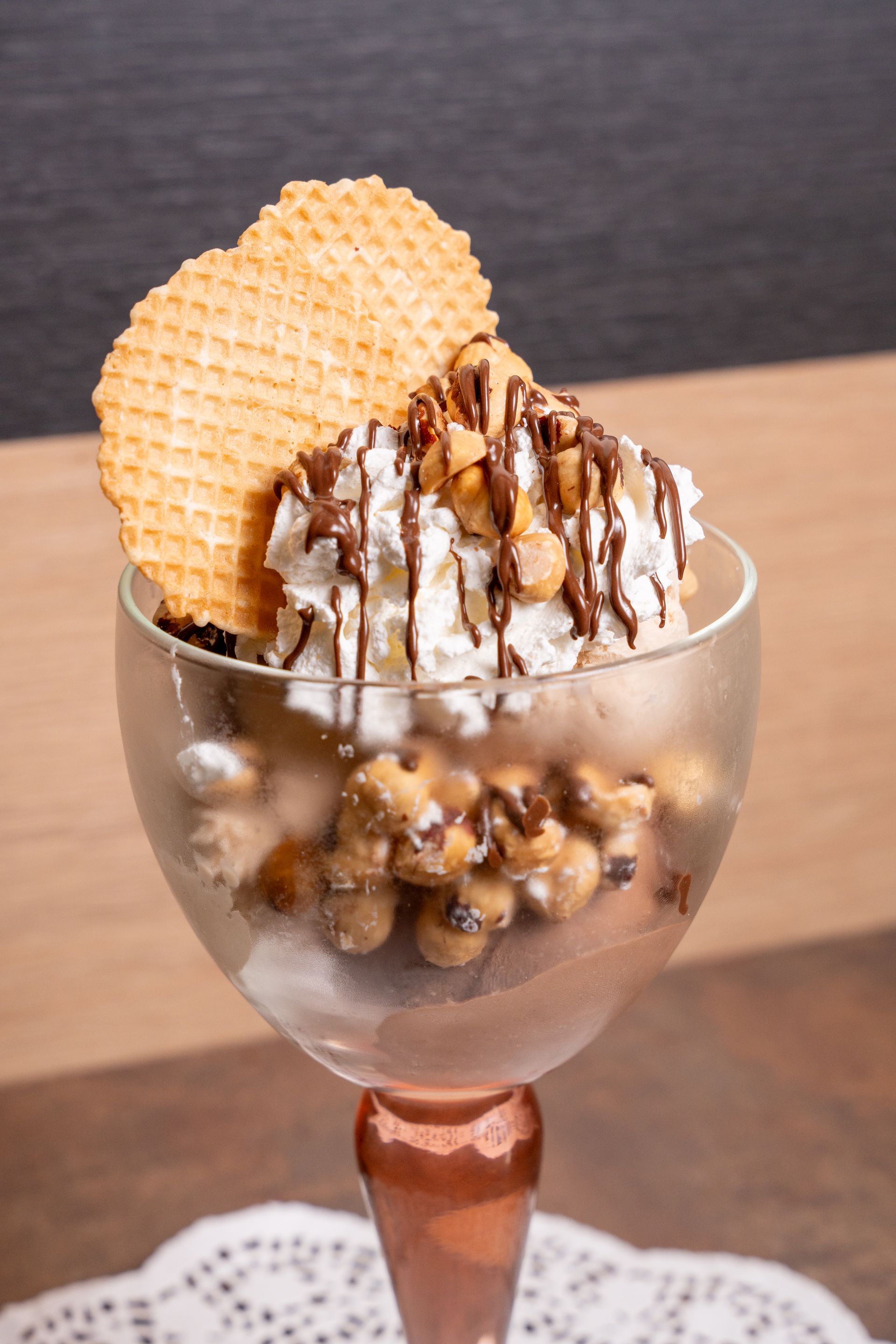 Coppa gelato in calice di vetro con biscotto waffle, panna montata e salsa al cioccolato.