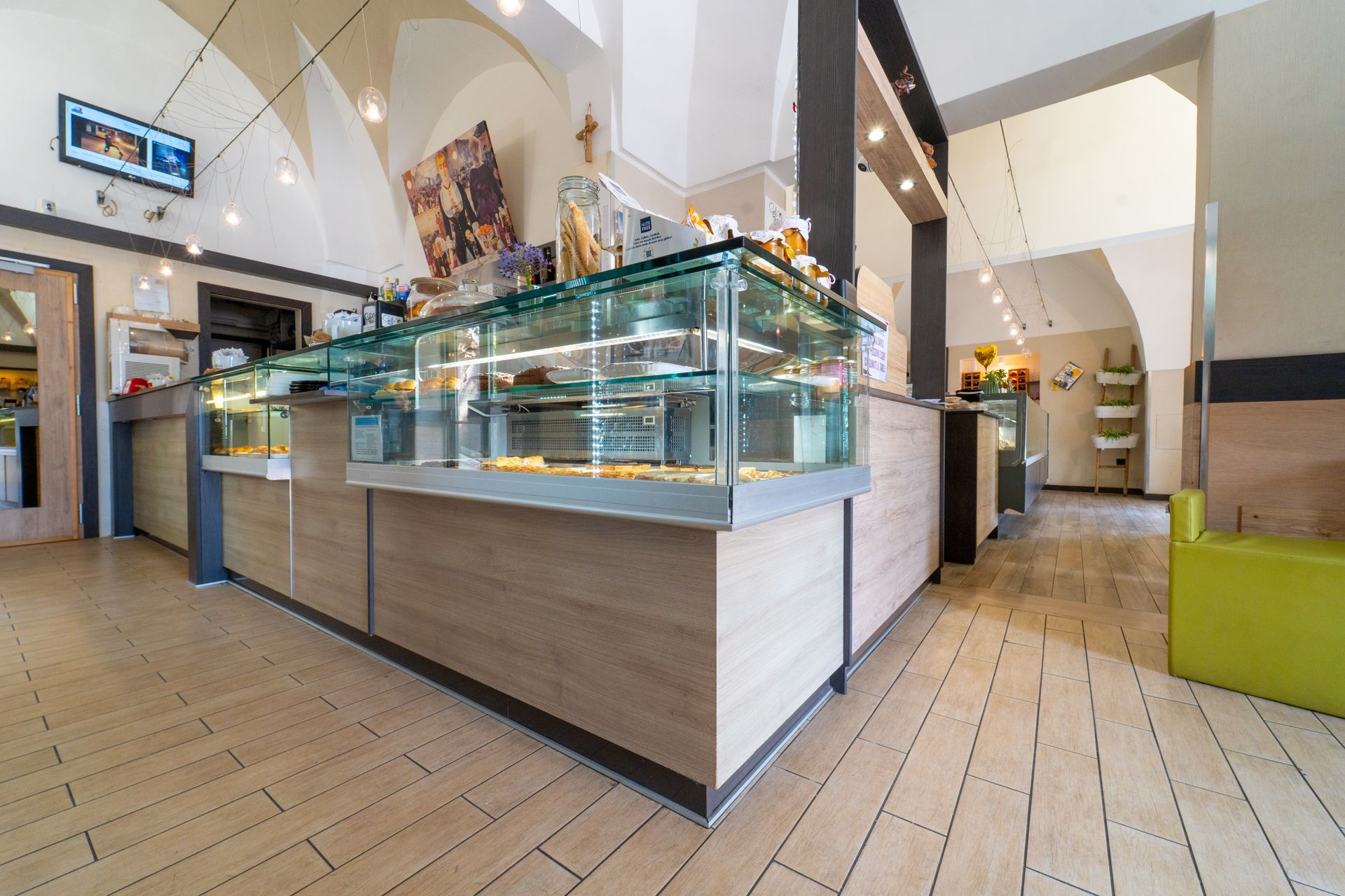 Interno moderno di una caffetteria con bancone in vetro per la pasticceria e pavimento piastrellato, illuminato da luminose luci a soffitto.