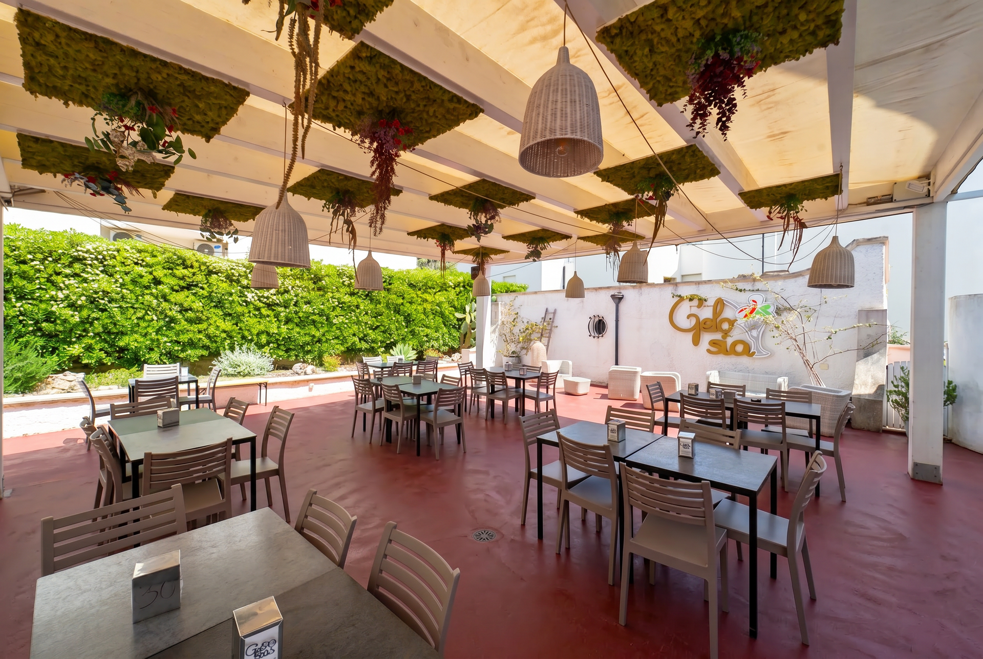 Ristorante con patio esterno, tavoli e sedie sotto una tettoia ombreggiata, immerso nel verde.
