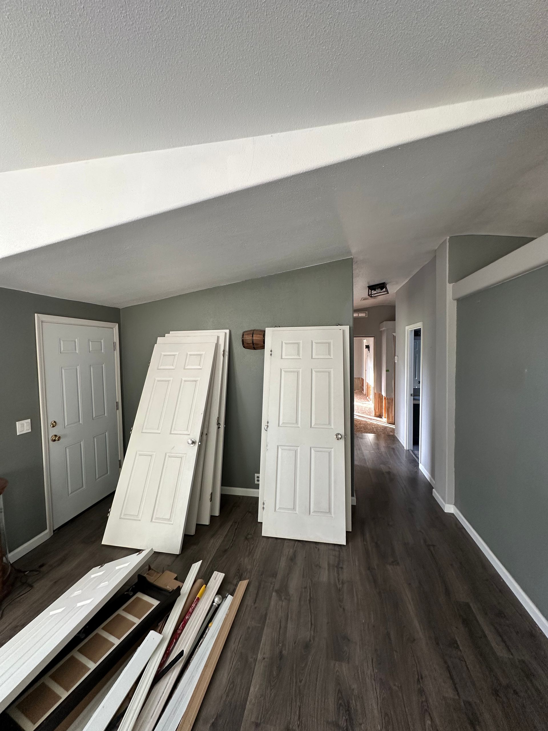 A gray room with a slanted ceiling and dark wood floors, featuring stacked white doors and construction materials.
