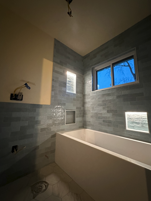 A square hole in a gray bathroom ceiling above a shower, exposing wall studs and insulation next to a white air vent.