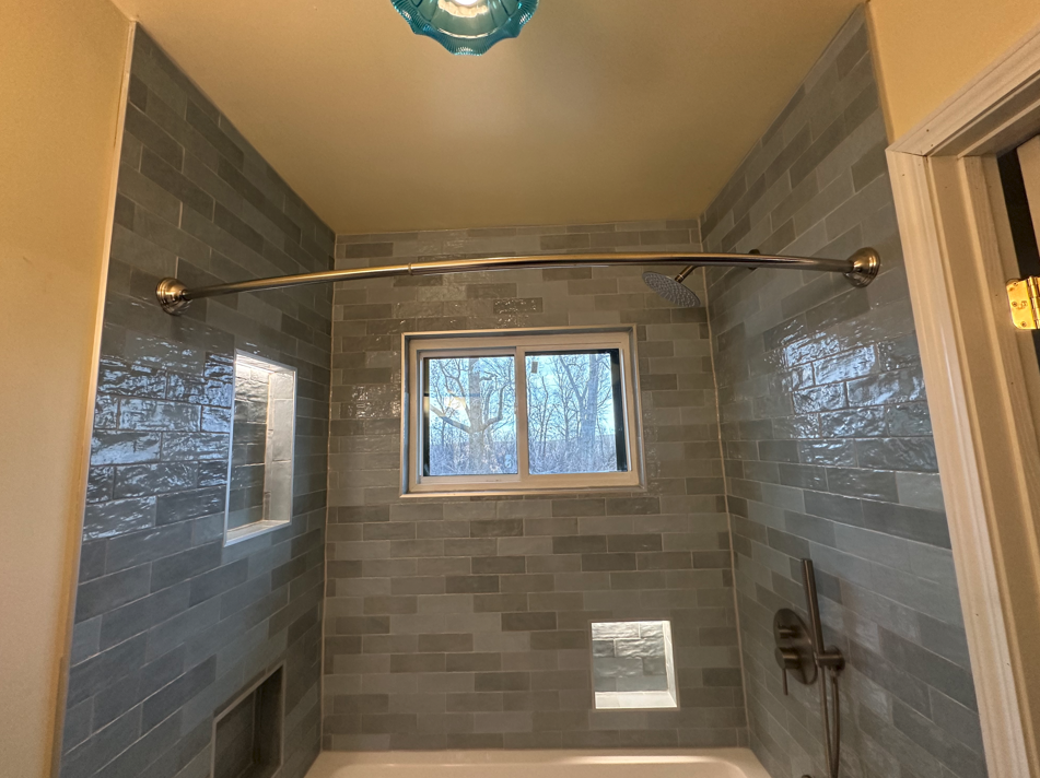 A square hole in a gray bathroom ceiling above a shower, exposing wall studs and insulation next to a white air vent.
