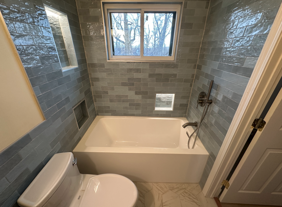 A square hole in a gray bathroom ceiling above a shower, exposing wall studs and insulation next to a white air vent.