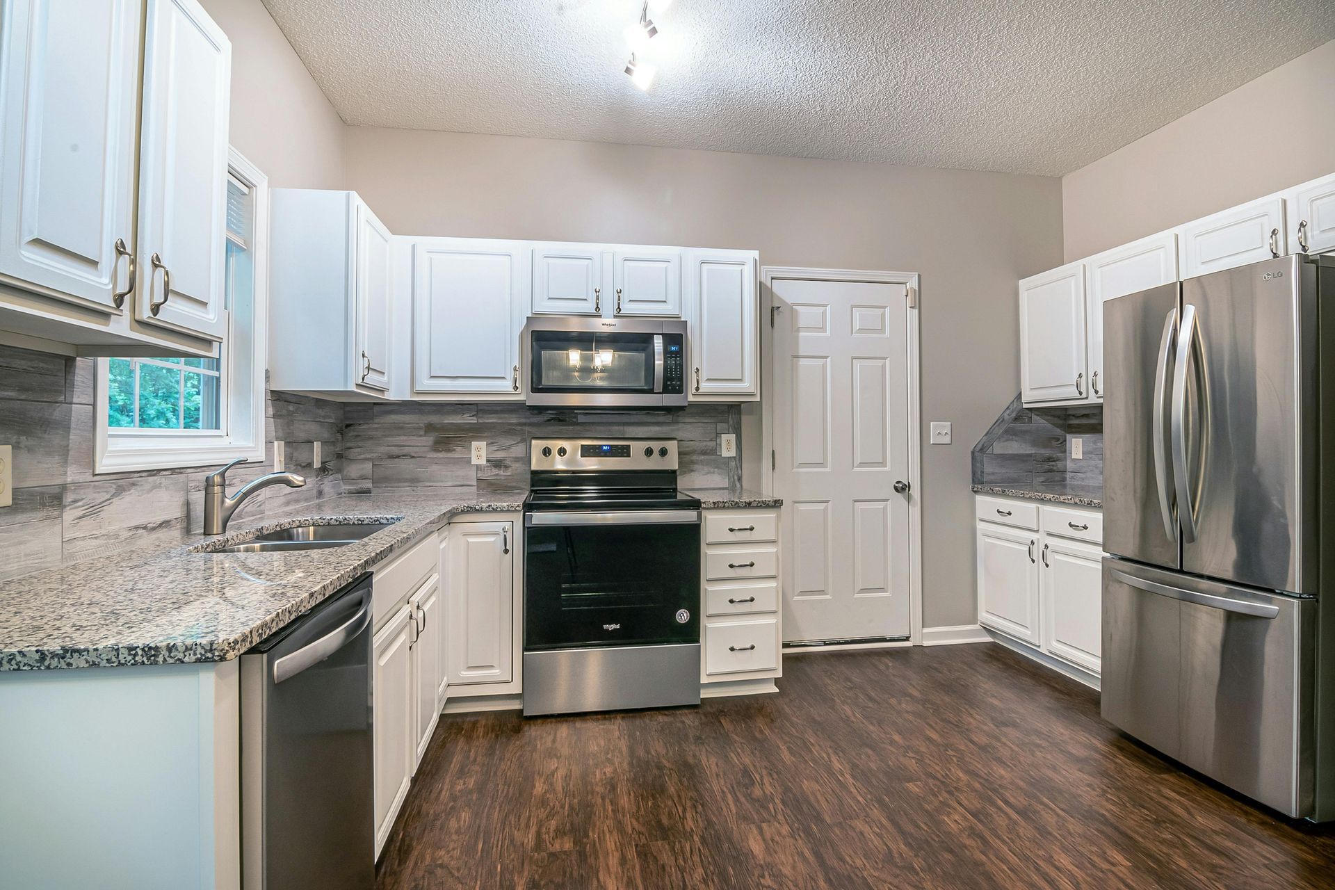 A kitchen with white cabinets, granite countertops, stainless steel appliances, and dark wood-look floors.