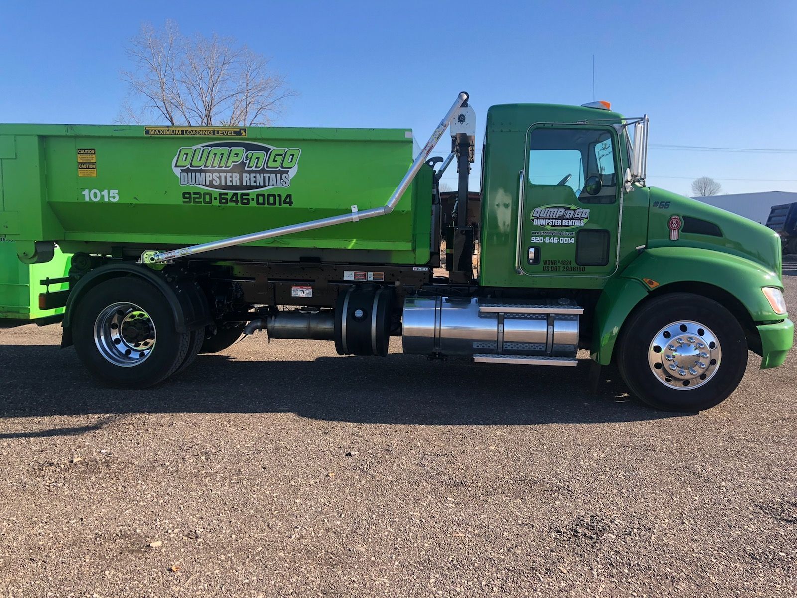 Green dump truck, parked on gravel, with a raised bed.