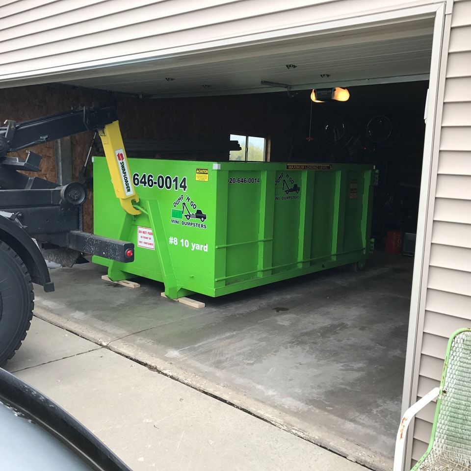 Green dumpster inside a garage being lowered by a tow truck.