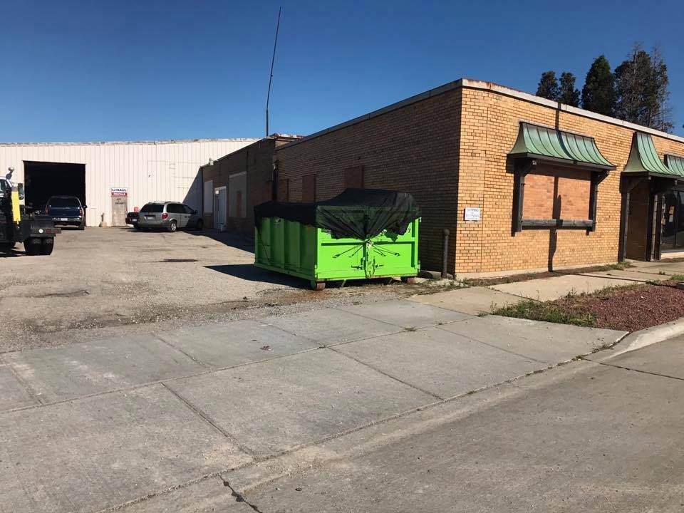 Exterior view of a commercial building with brick facade, a green dumpster, and a white metal building attached.