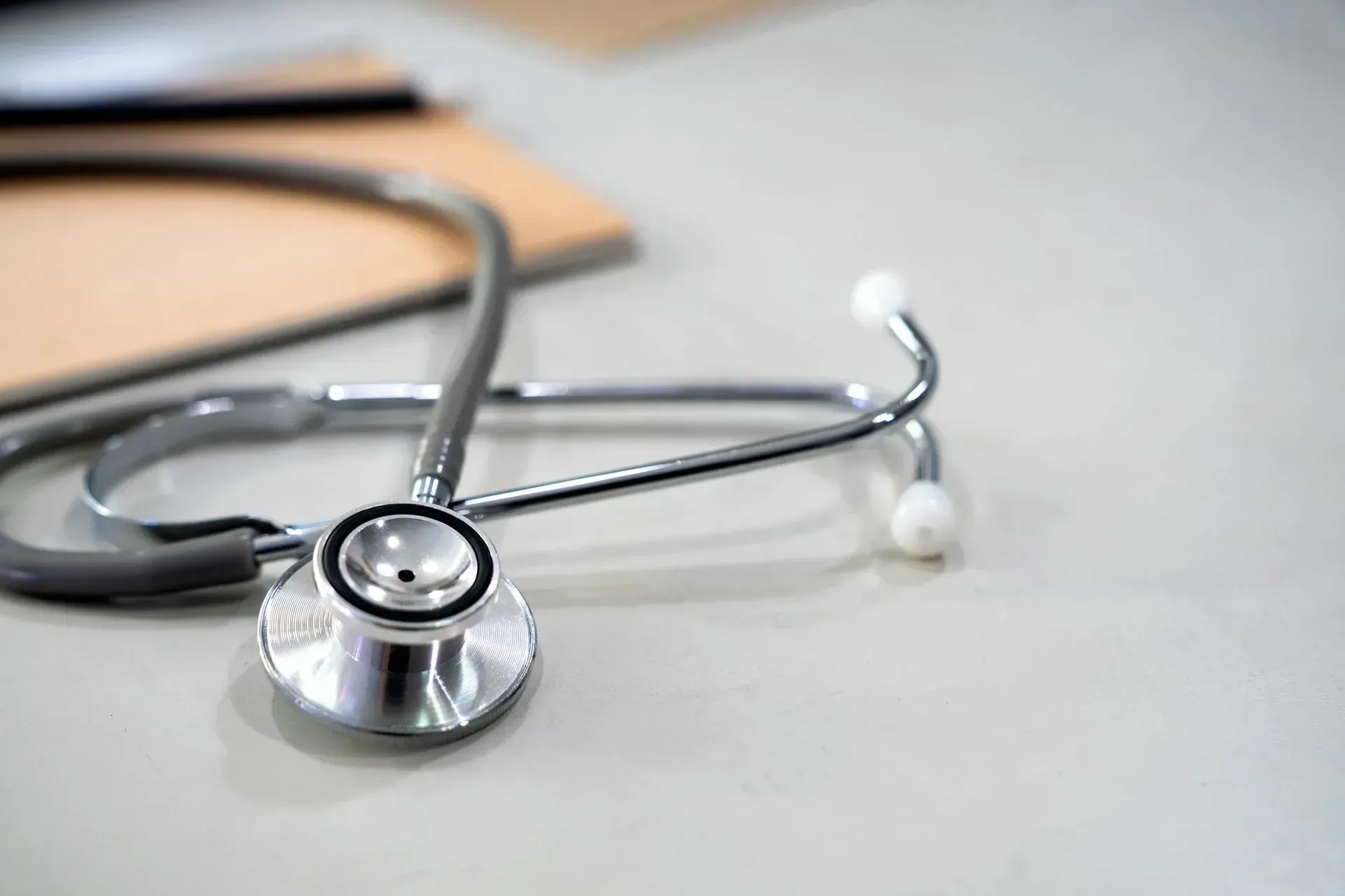 A stethoscope is sitting on a table next to a clipboard. A stethoscope is sitting on a table next to a clipboard.