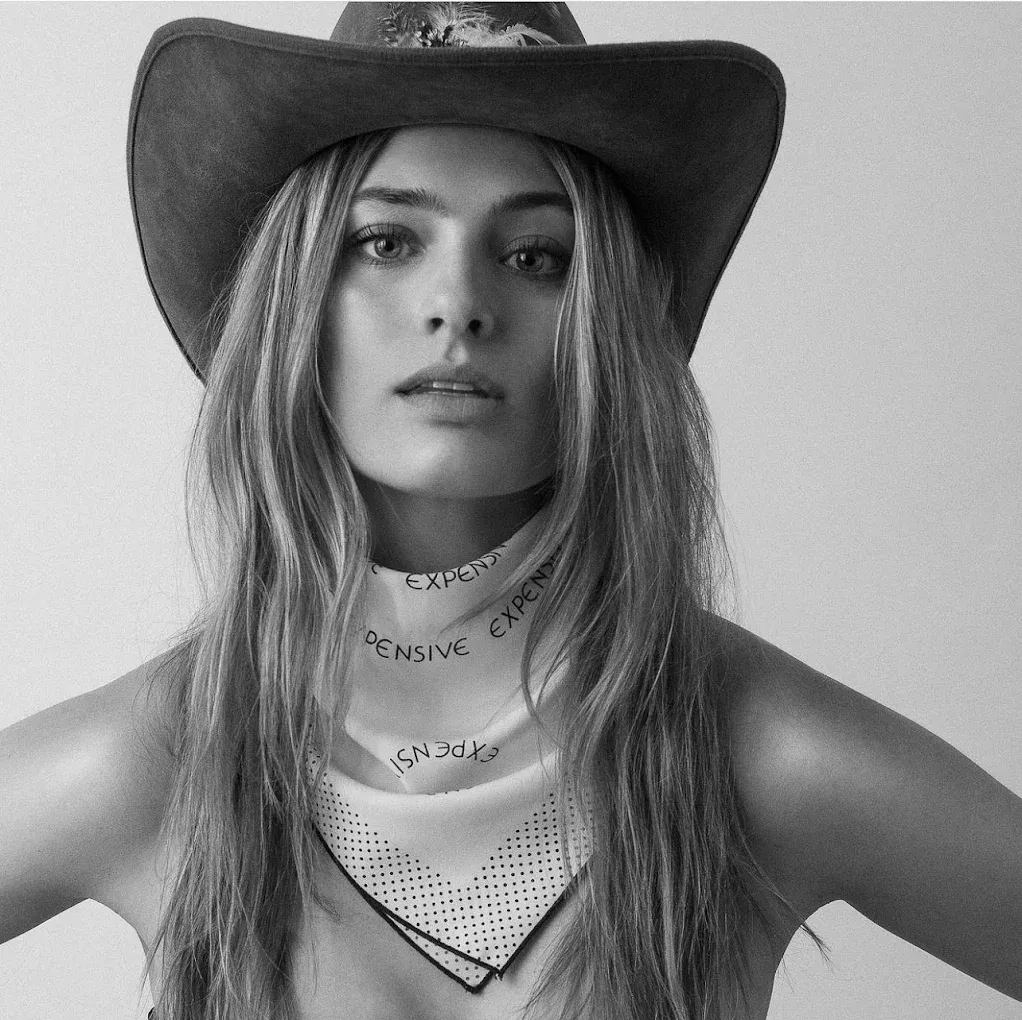 Woman wearing cowboy hat and neck scarf, looking directly at the viewer in a grayscale portrait.