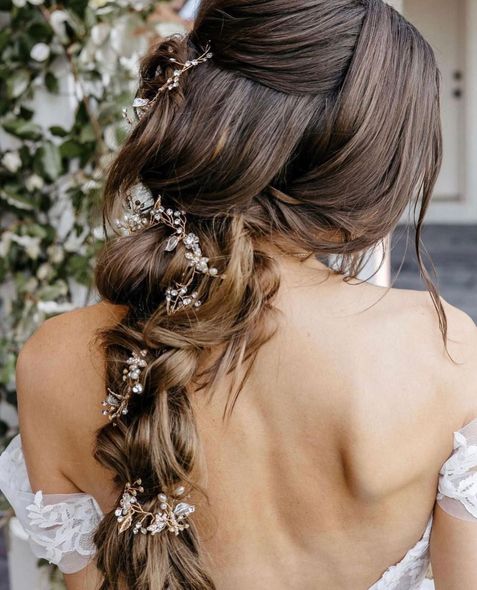 Woman's back with brown hair styled in a braid, adorned with jeweled hair accessories; wearing a white lace dress.