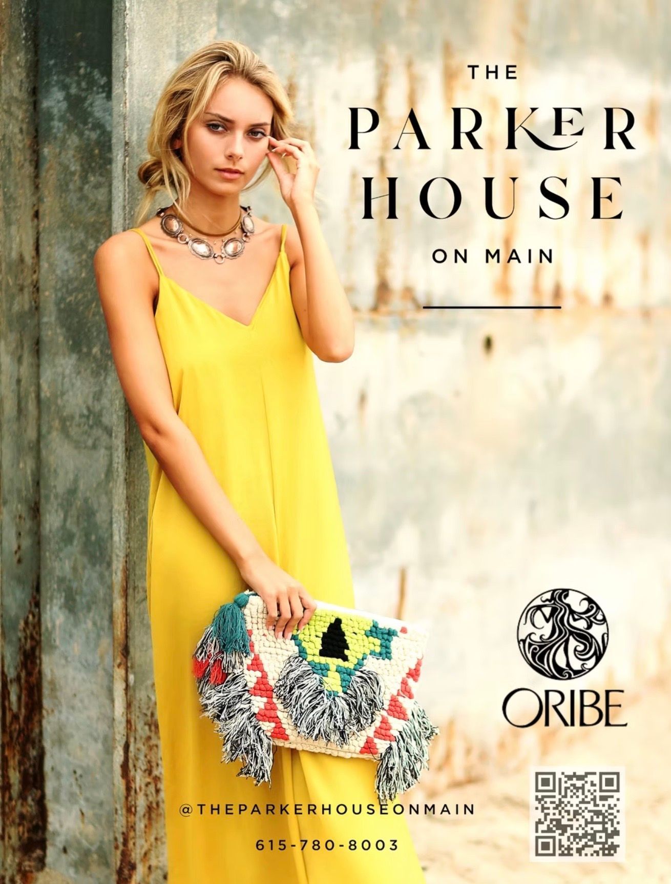 Woman in yellow dress holding a colorful clutch, standing in front of a wall. Advertisement for The Parker House On Main.