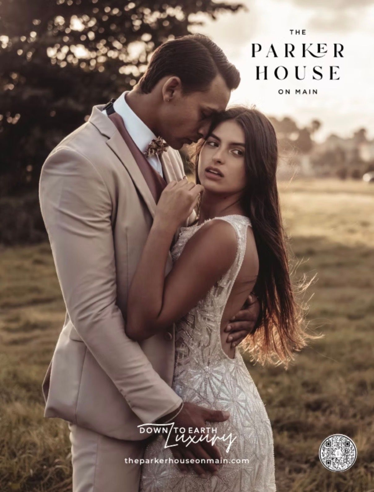 Couple embracing outdoors, man in tan suit kissing woman's head, she wears white gown; 