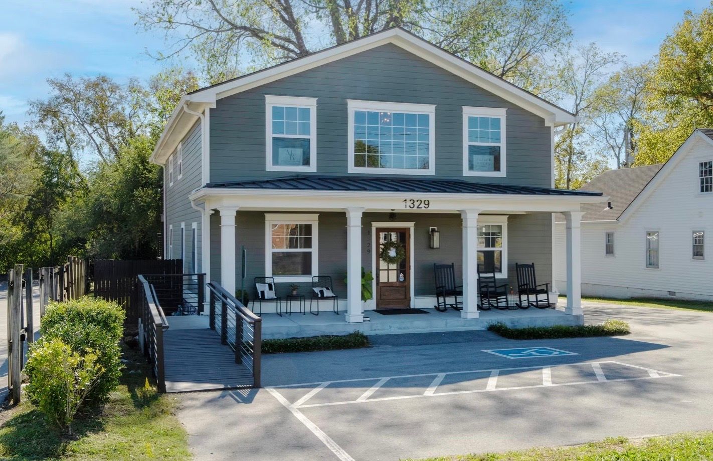 Two-story gray building with porch and wheelchair ramp, parked cars, and trees, with the number 1321 above a brown door.