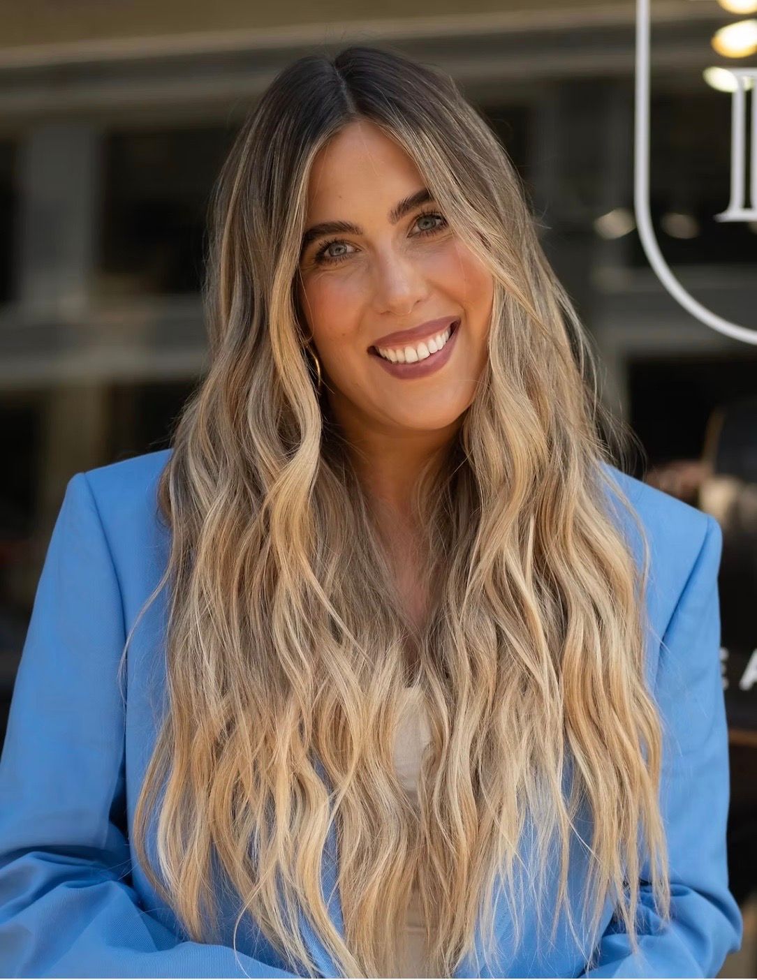 Woman with long blonde hair smiles in a light blue blazer.