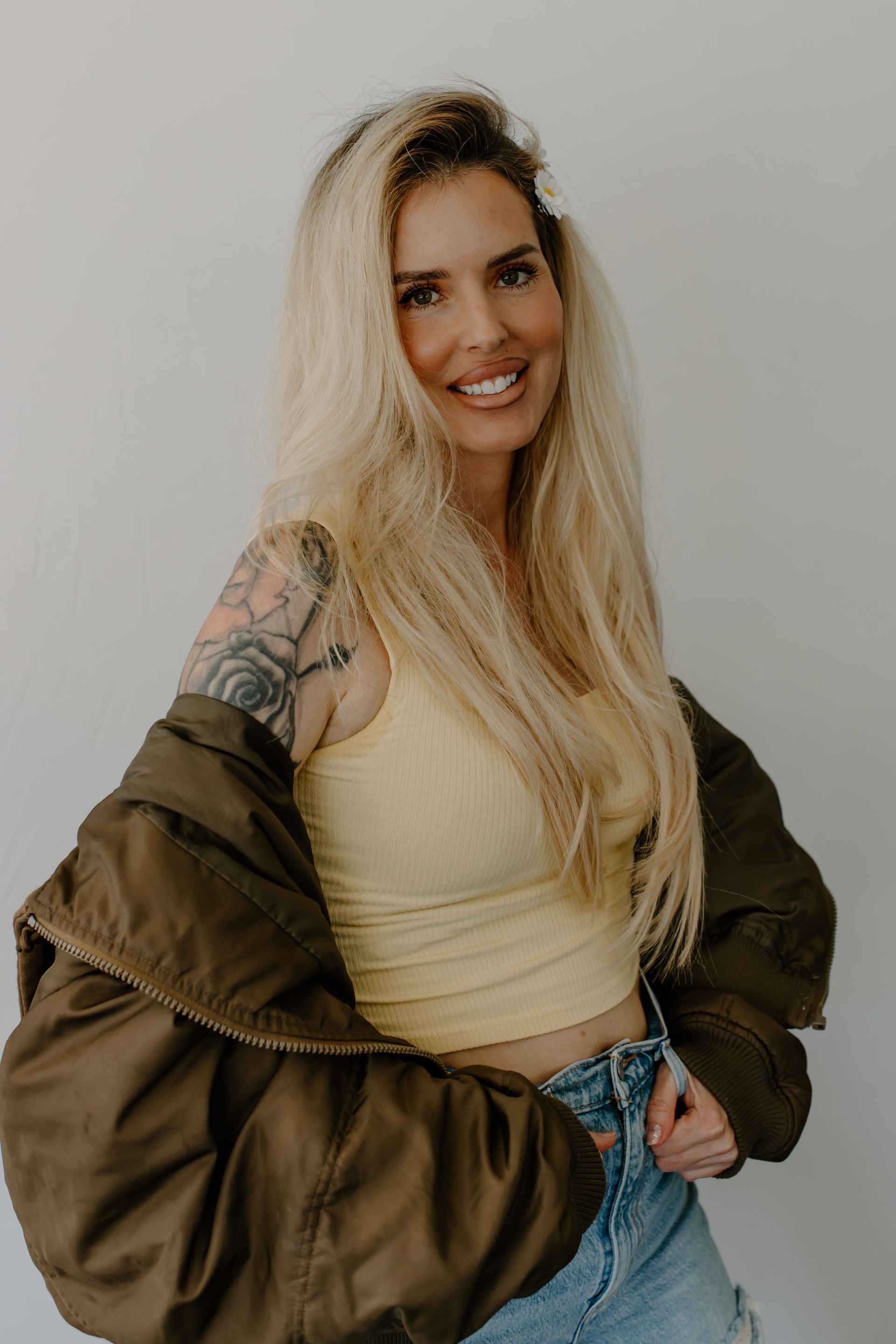 Young woman with blonde wavy hair smiles, wearing a gray top, small silver necklace, indoors.