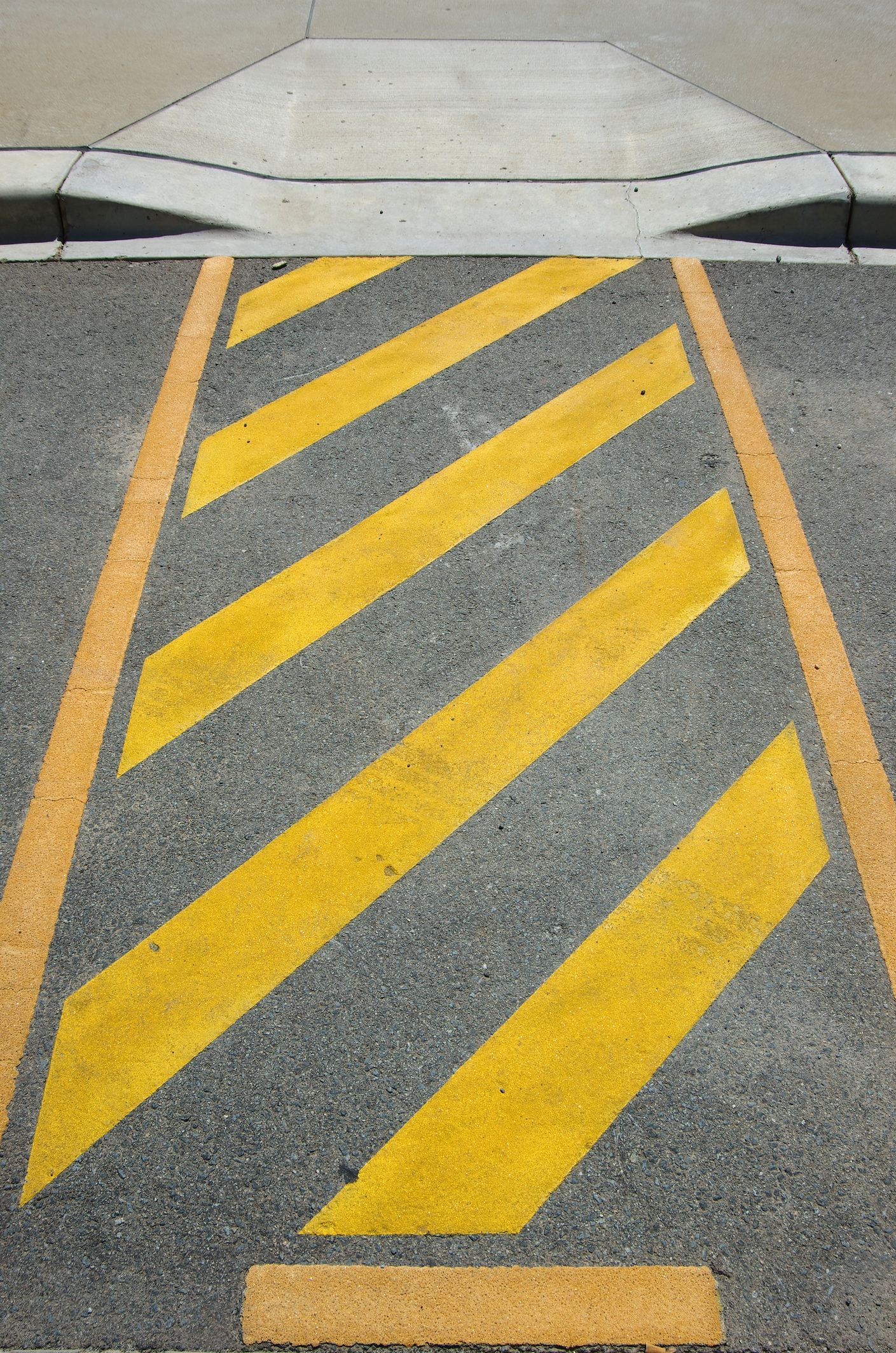 Yellow diagonal stripes within yellow borders on asphalt, adjacent to a curb.