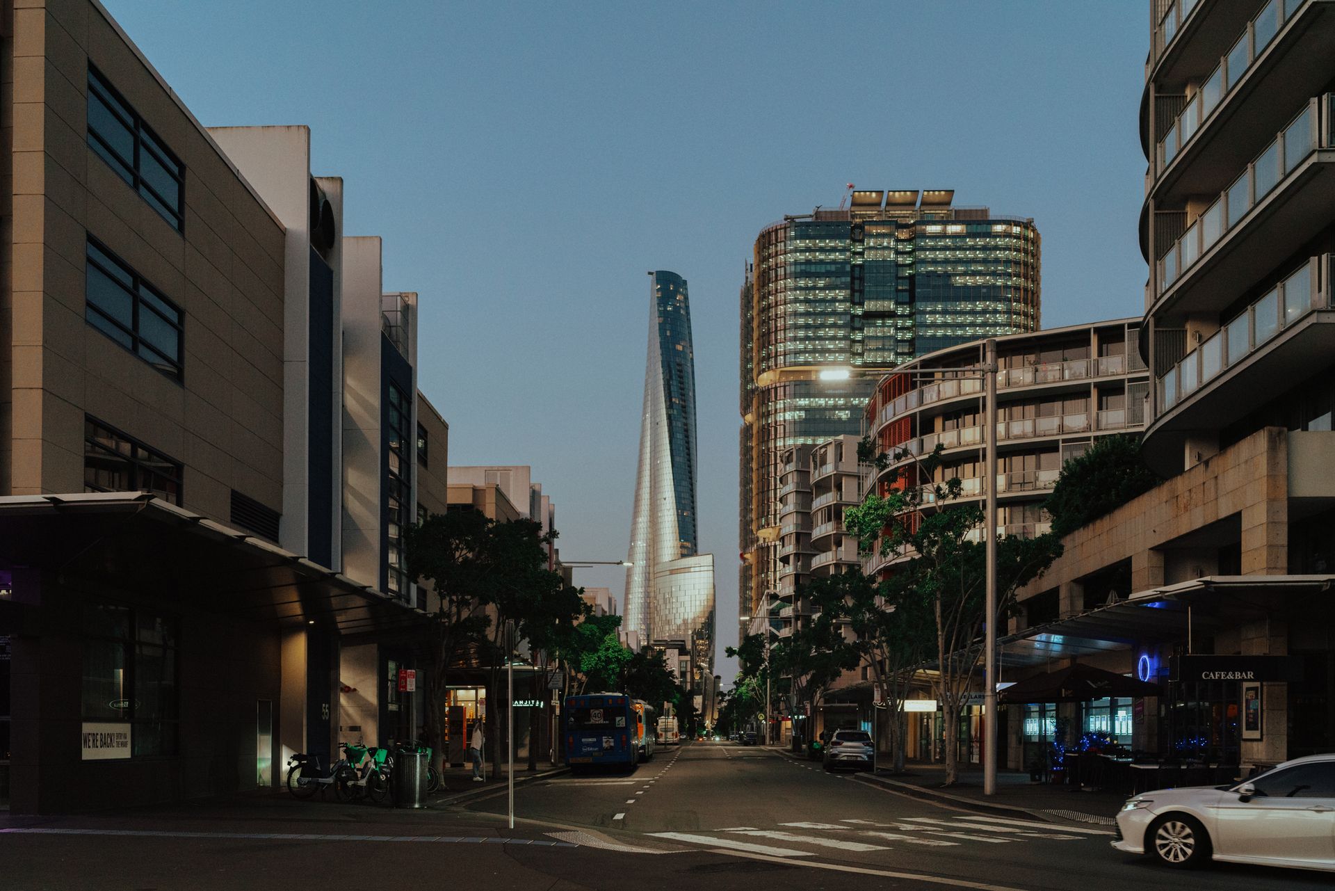 Street view with tall modern buildings, including a curved, white skyscraper at the end of the road.
