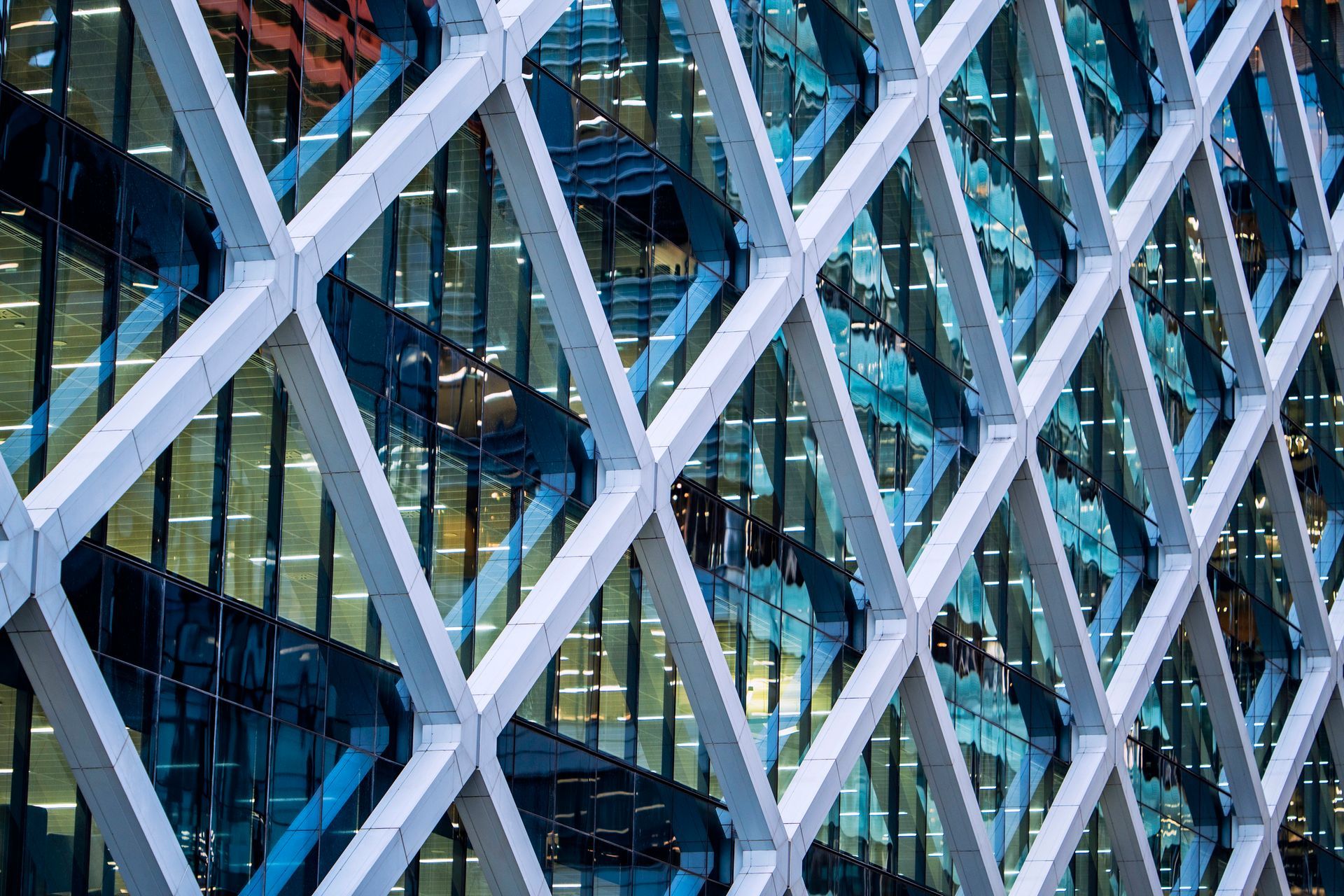 White diamond-patterned metal facade over a glass skyscraper with blue and gold reflections.
