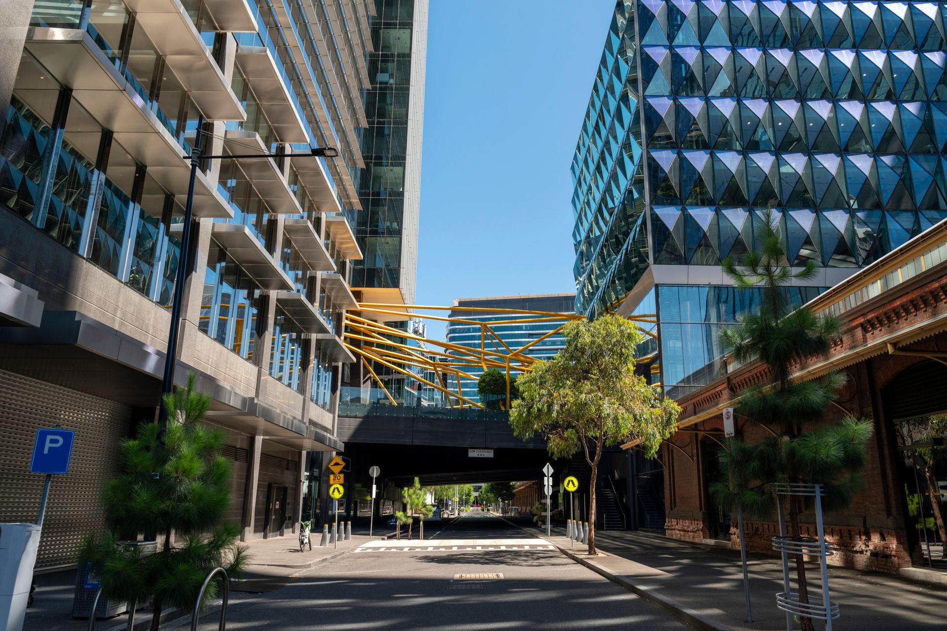 Street view between modern buildings; bridge in distance, blue sky.
