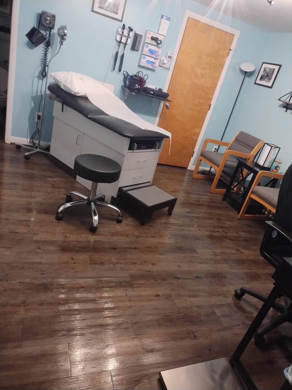A doctor 's office with a examination table , chairs , and a stool.