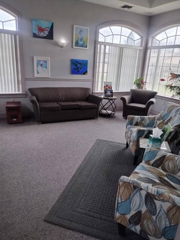 A living room with a couch , chairs , and paintings on the wall.