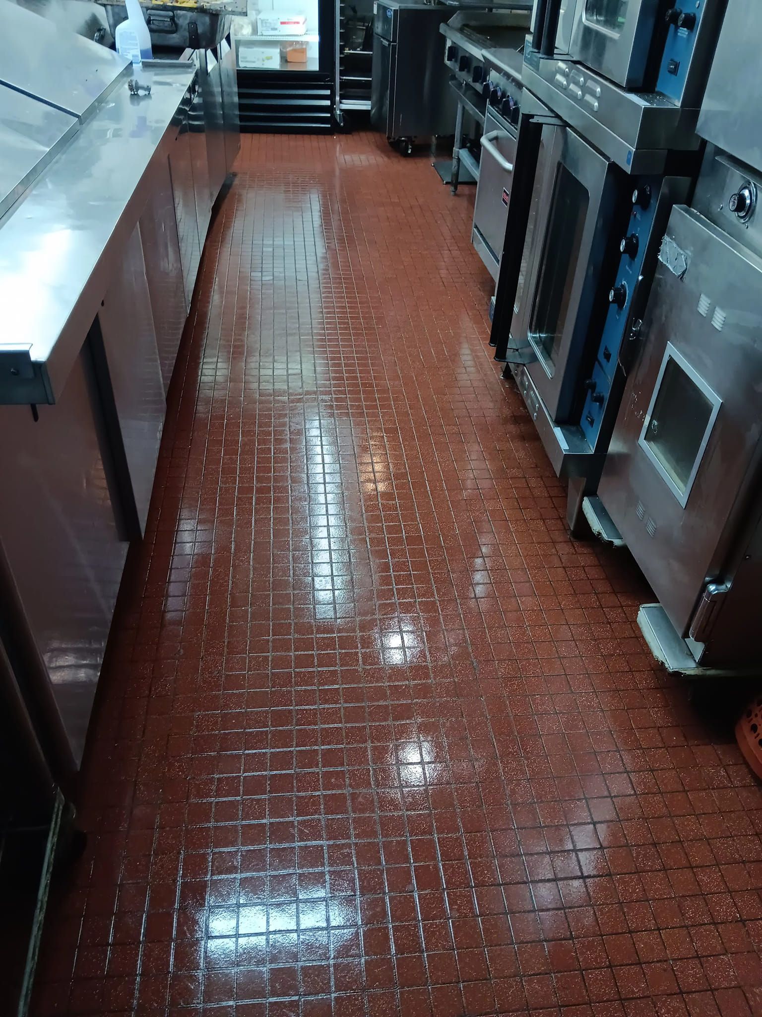 A kitchen with a red tile floor and stainless steel appliances.