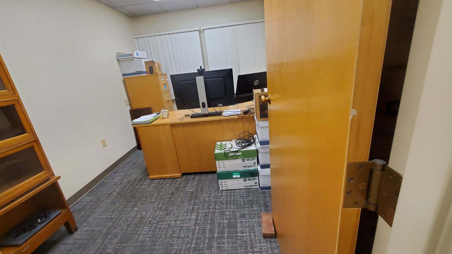 A room with a desk , two computers , and a door.