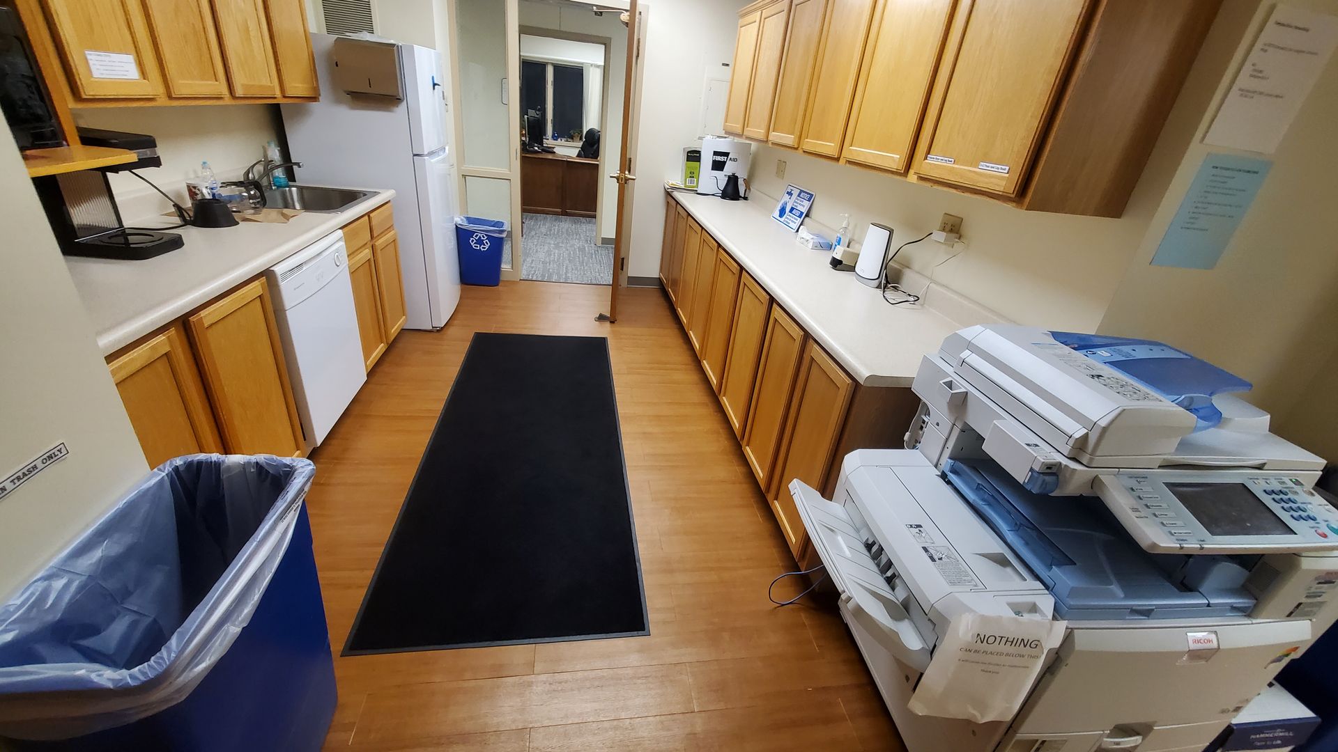 A kitchen with wooden cabinets , a trash can , and a printer.