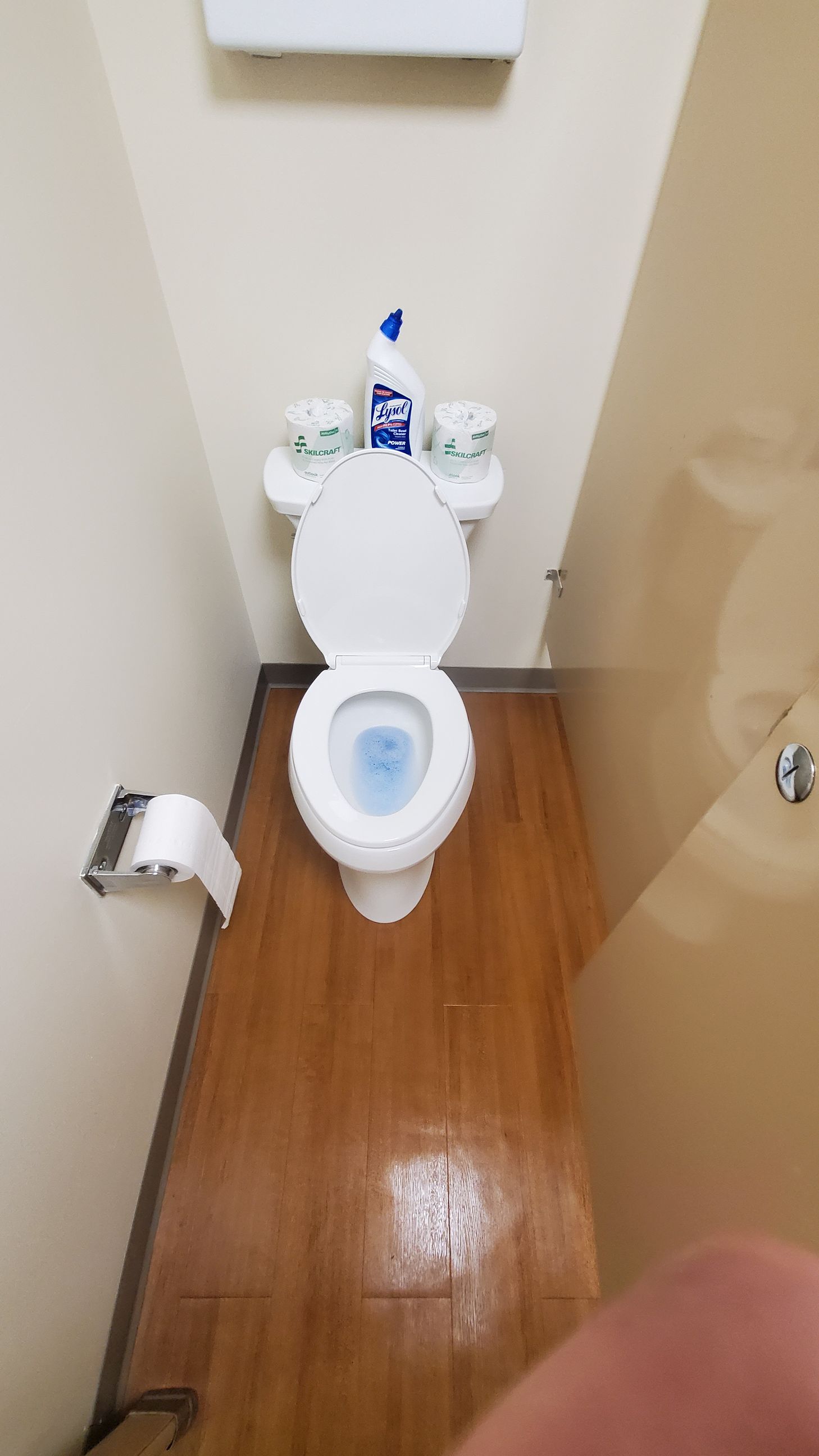 A toilet is sitting on a wooden floor in a bathroom.