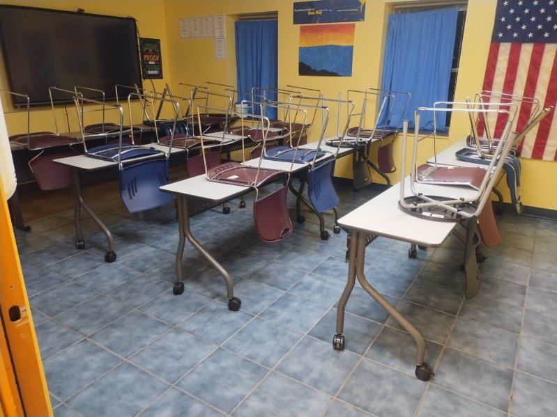 A classroom with tables and chairs and an american flag on the wall