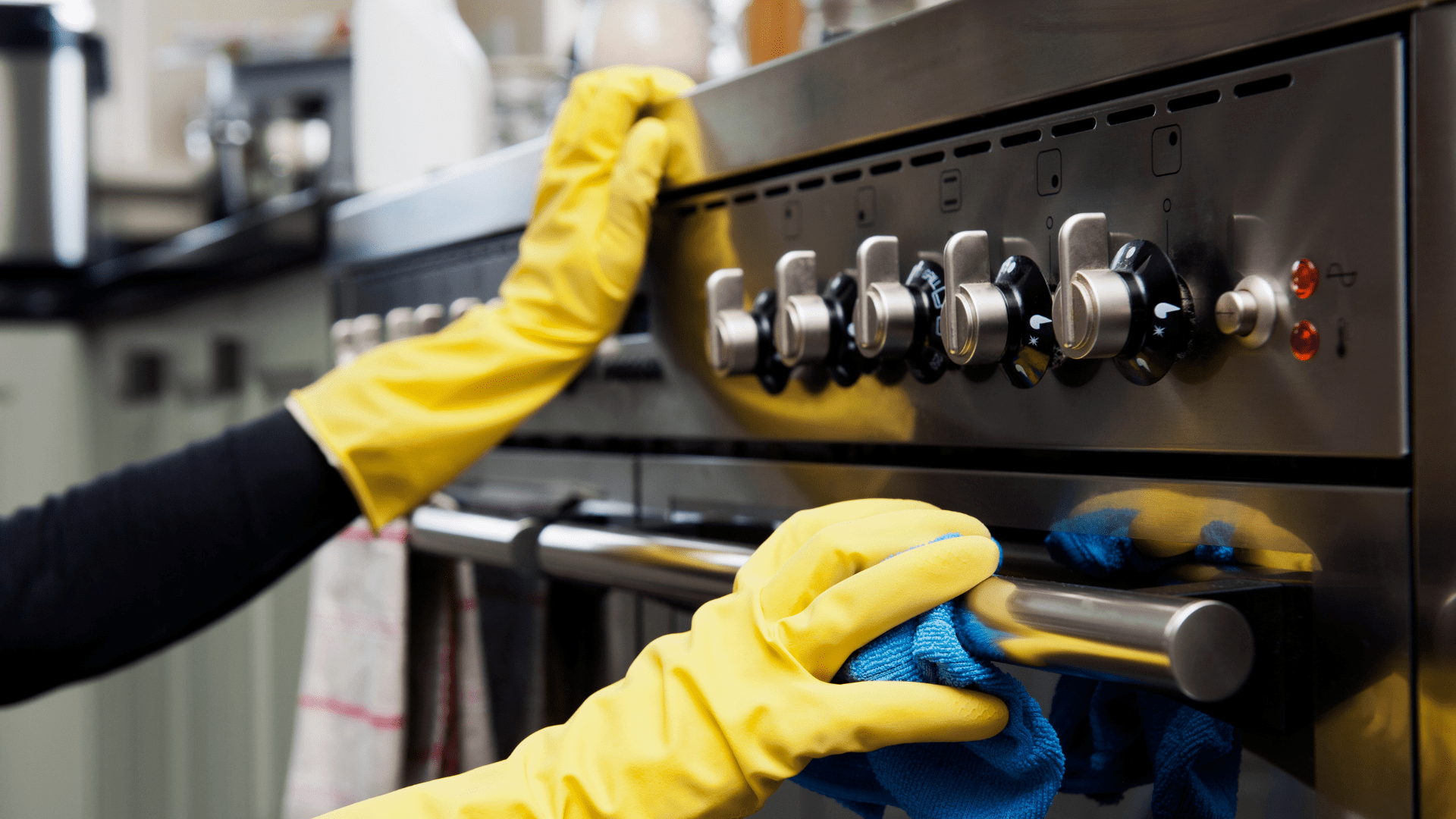 A person wearing yellow gloves is cleaning a stove with a cloth.