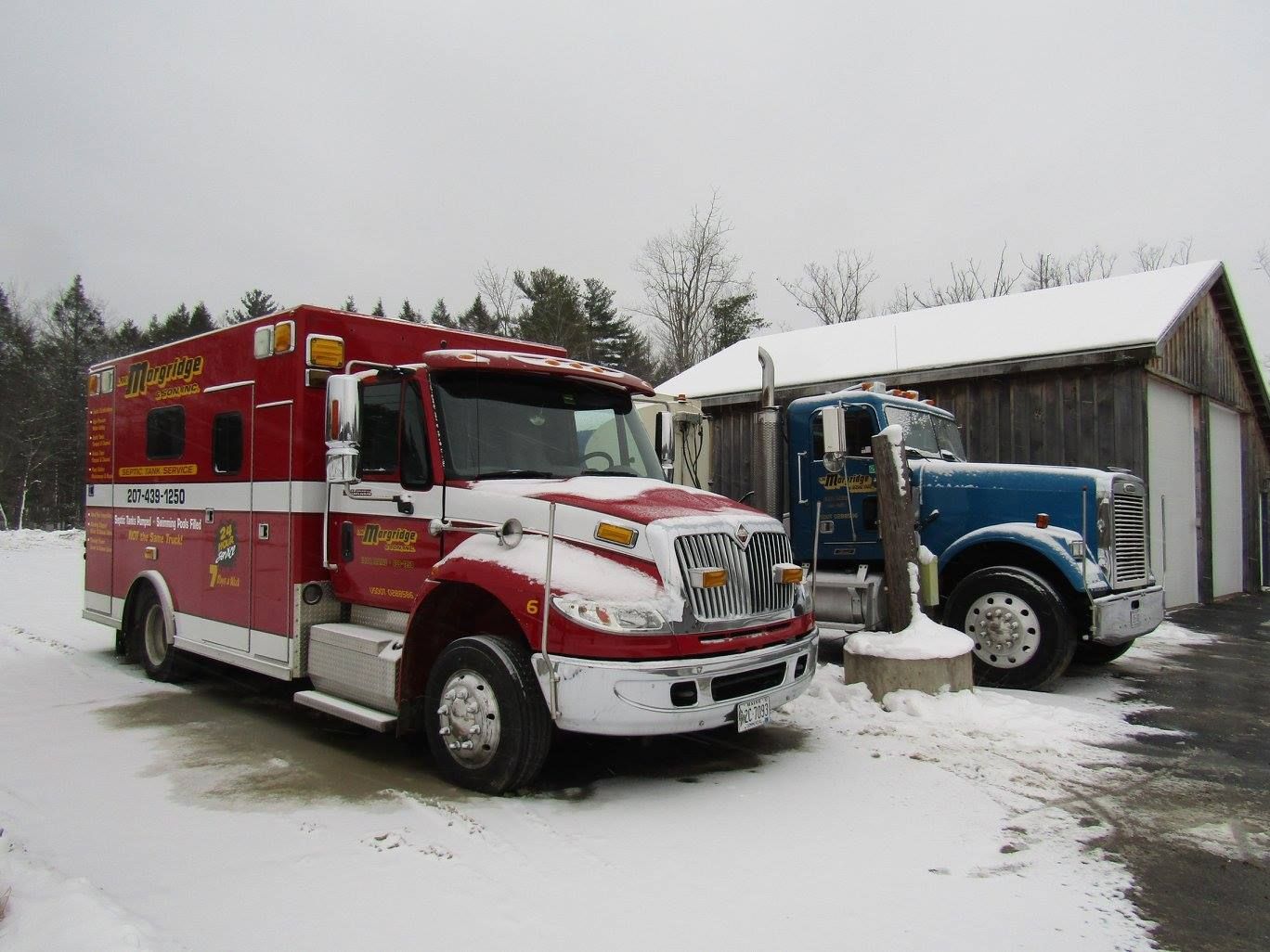 A red ambulance is parked next to a blue truck in the snow.