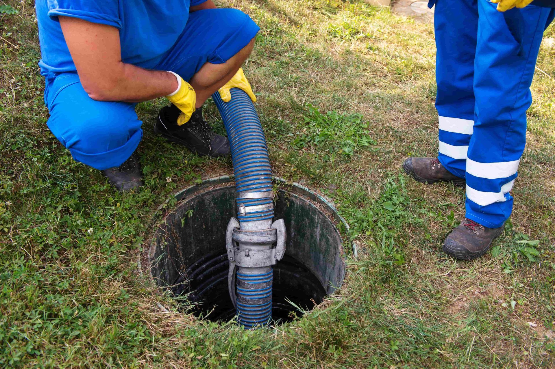 A man is kneeling down next to a manhole cover with a hose coming out of it.
