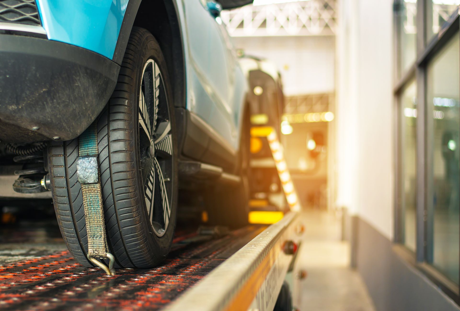 Close-up of a wheel strap used by a car towing service to secure a light blue car on a trailer.