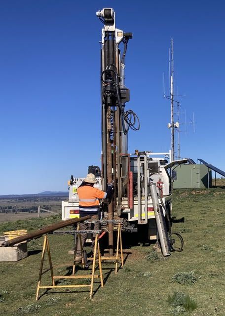 Two men are working on a drilling machine in a field.