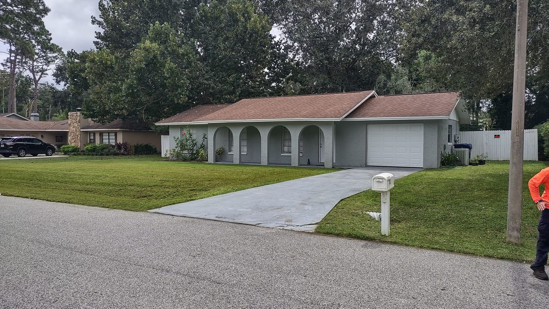 Ranch-style house with brown roof and green lawn; gray driveway and mailbox in front.