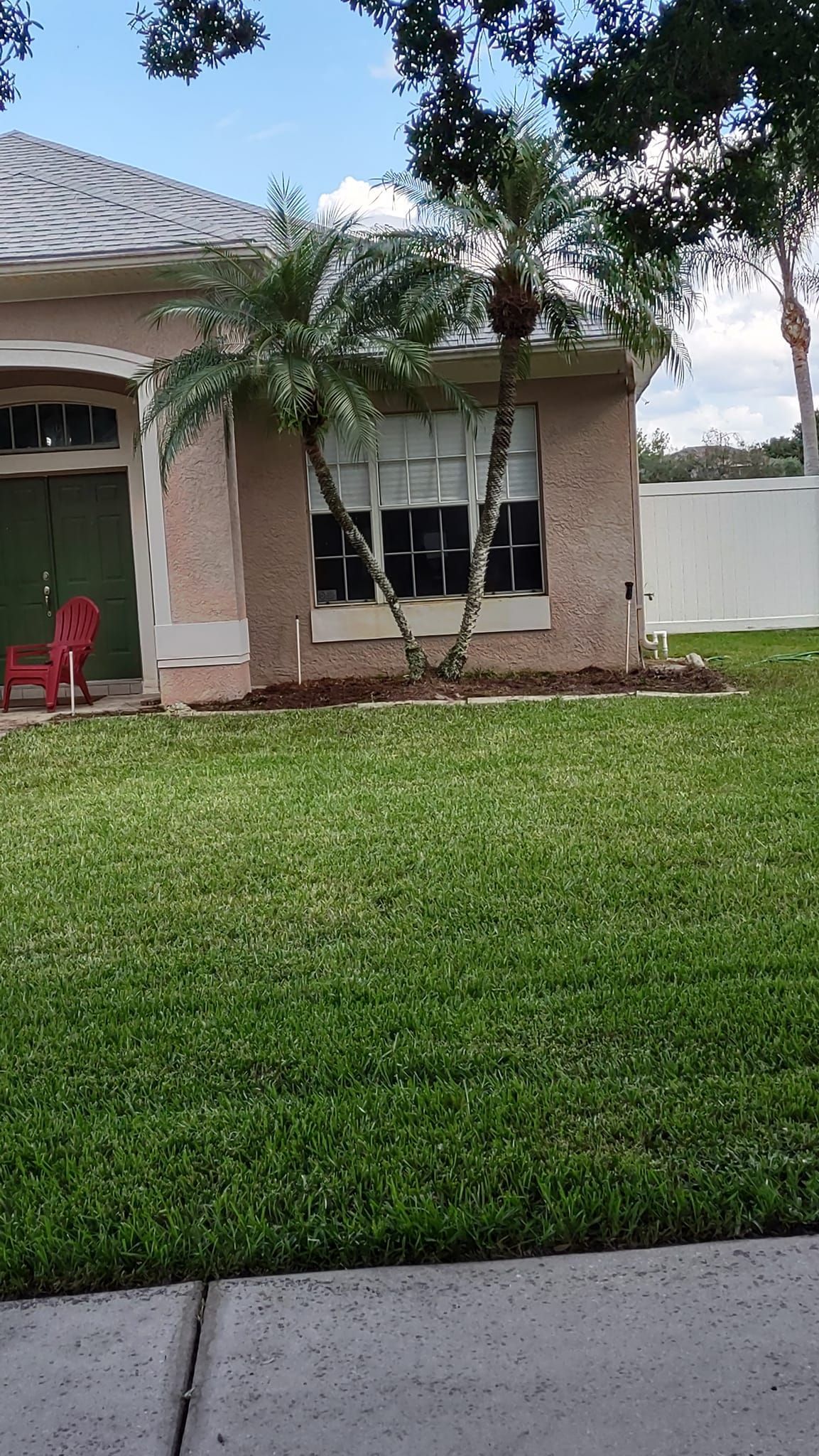 A house with green lawn and a tree in front, red chair on porch.