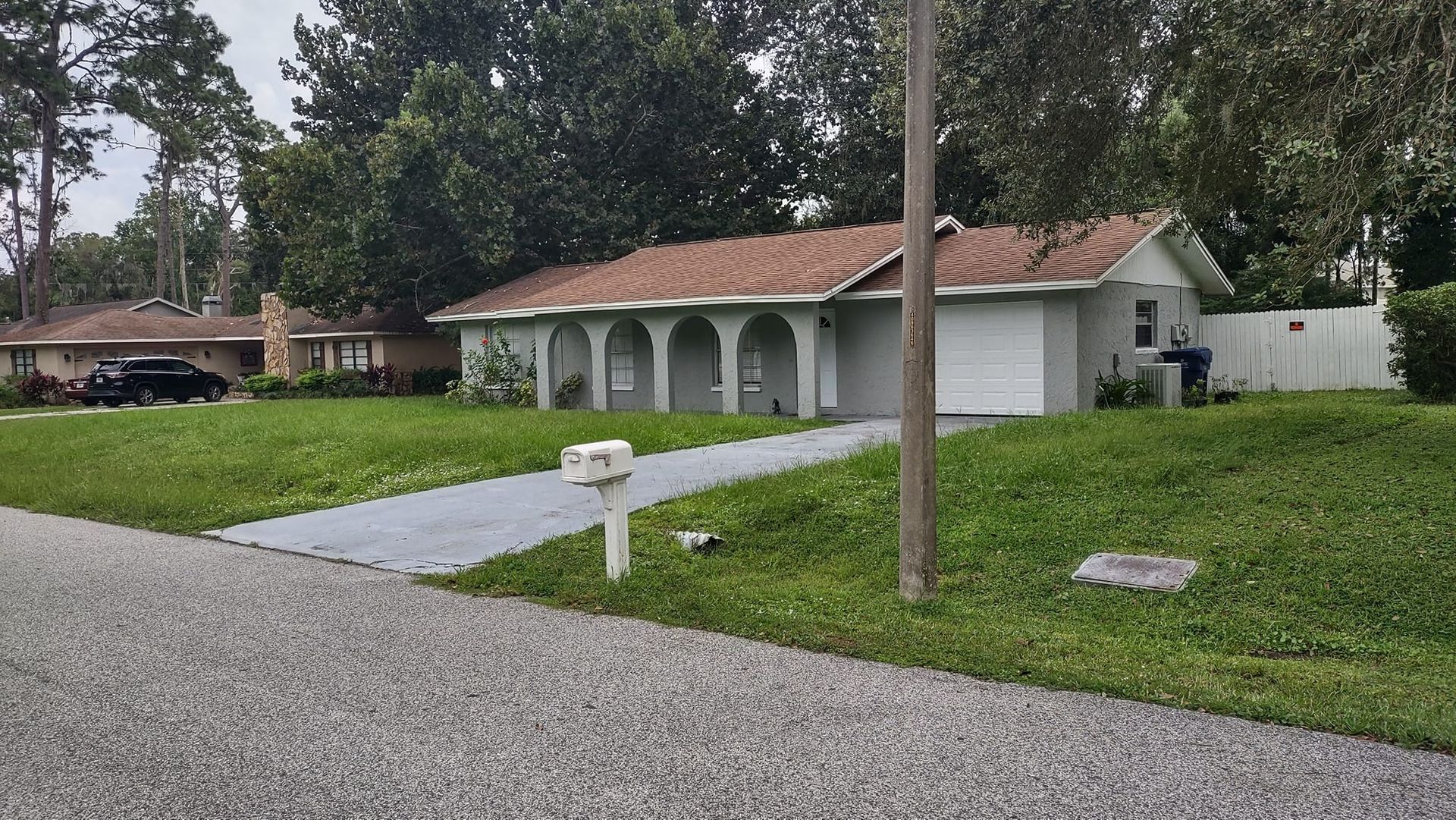 A light-blue house with a brown roof and archway porch, next to a driveway and mailbox, on a green lawn.