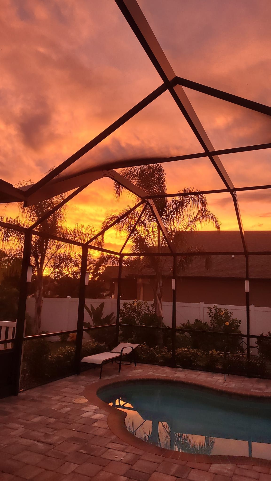 Sunset over a pool and screen enclosure; sky ablaze with orange and pink hues.