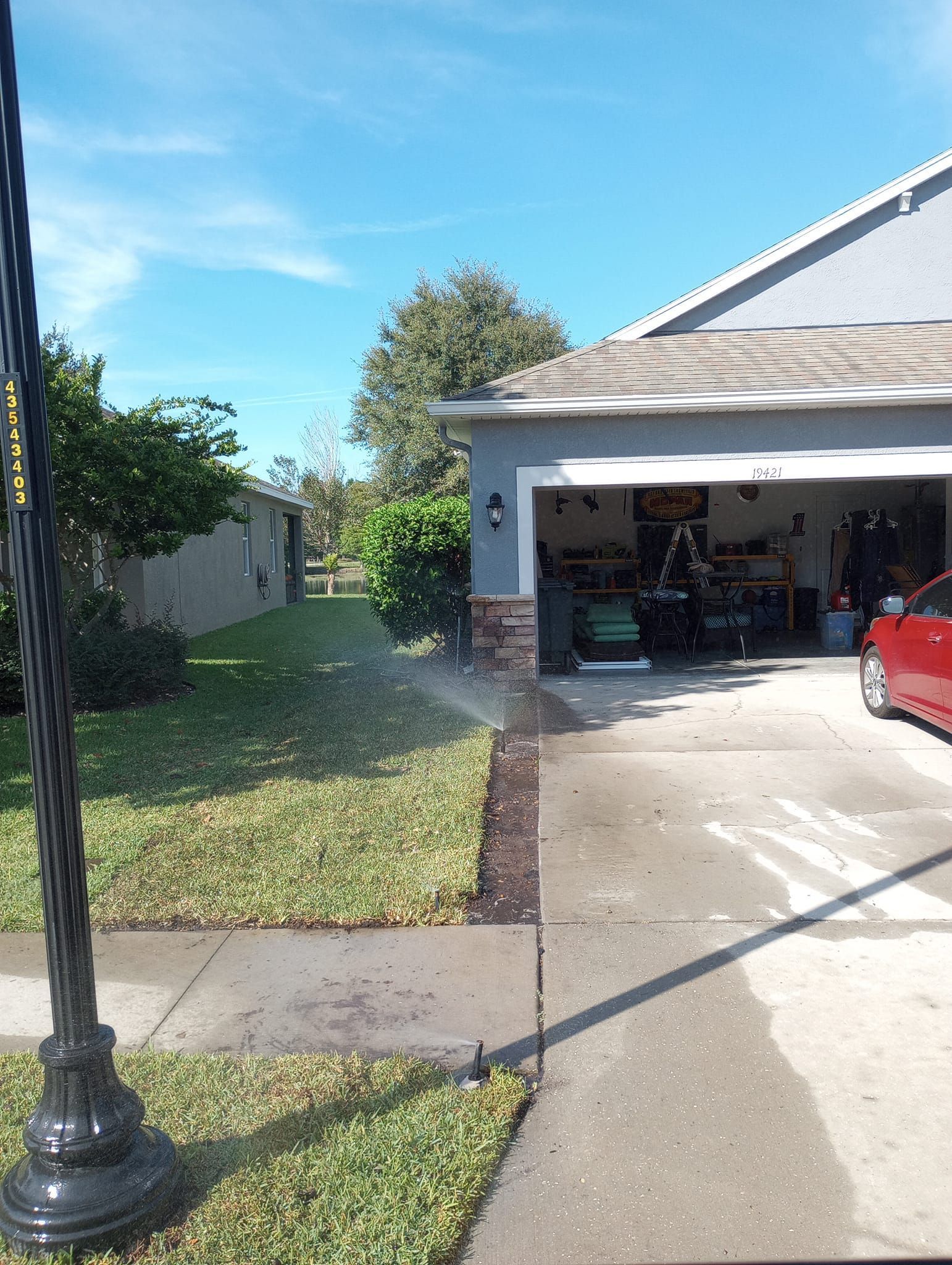 A sprinkler waters the front yard of a house with a garage door open on a sunny day.